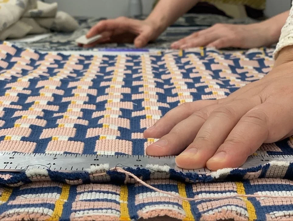 Close-up of Ruti measuring a woven textile with a ruler, with hands pressing the fabric onto the ruler for accuracy in her workshop