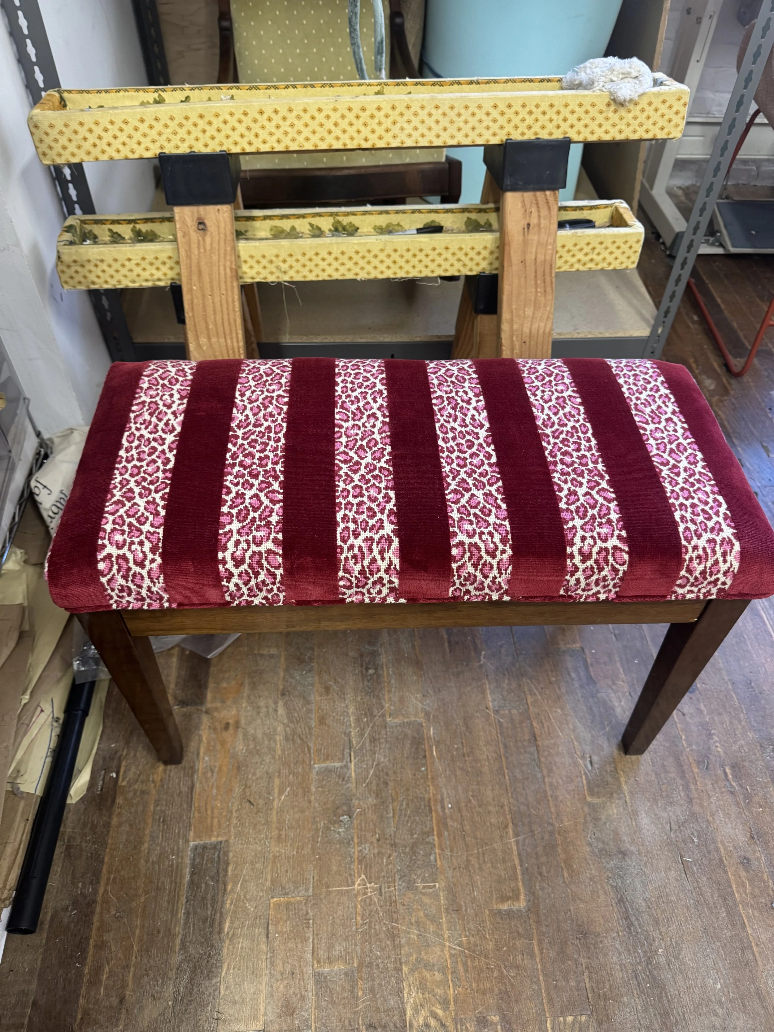 A wooden bench with a red and white patterned cushioned seat in a store.