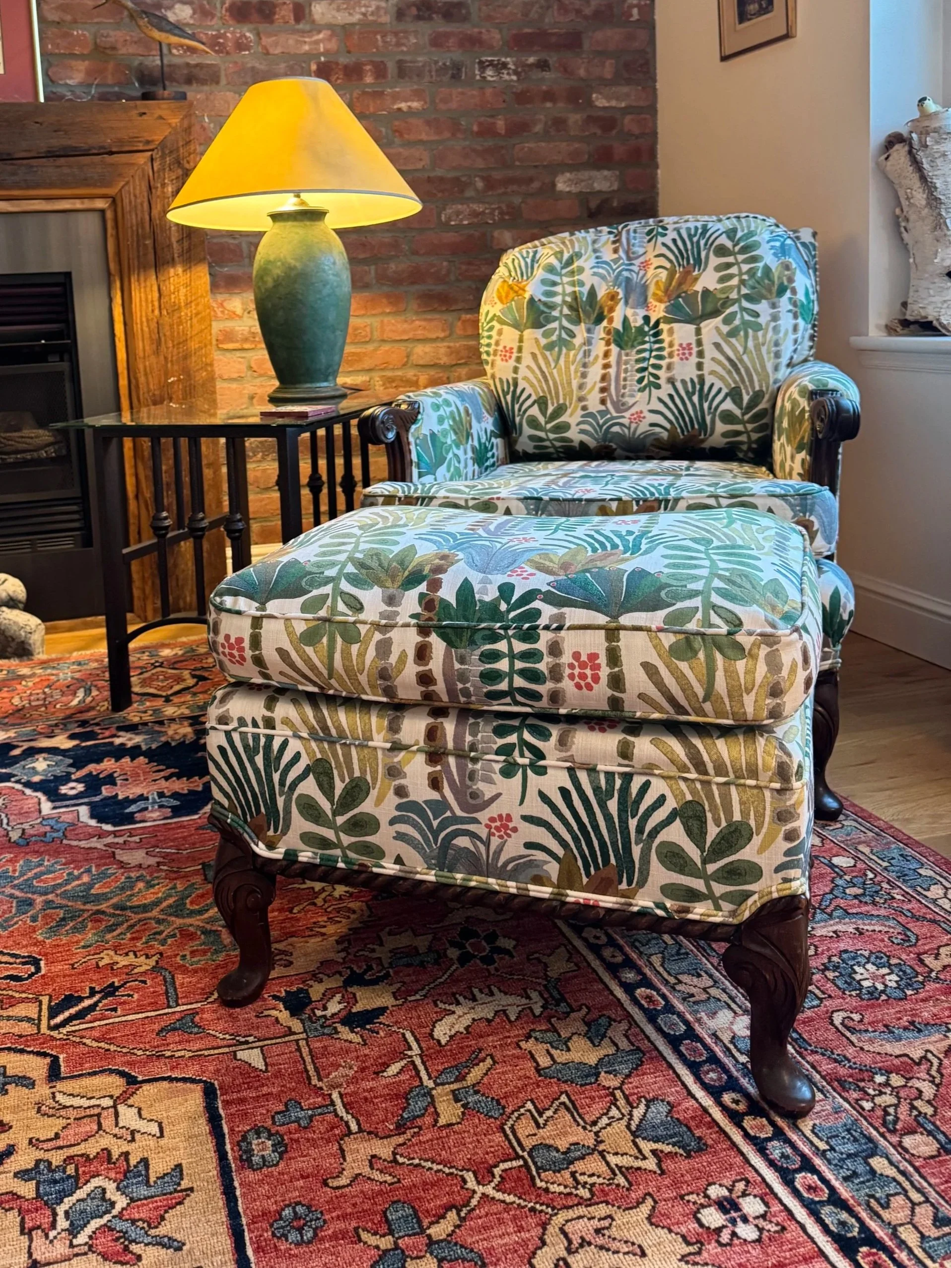 A cozy living room corner featuring a floral upholstered armchair and matching ottoman.