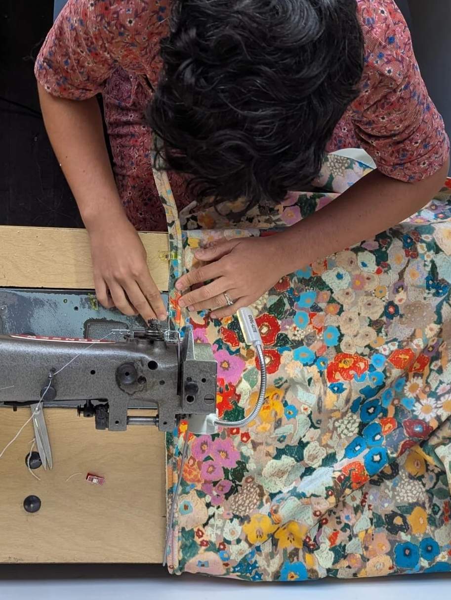 Ruti sewing a colorful floral fabric on a sewing machine.