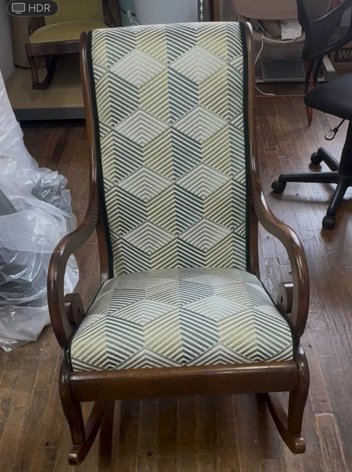 A vintage wooden armchair with geometric patterned upholstery in shades of green, beige, and black, placed on a wooden floor.