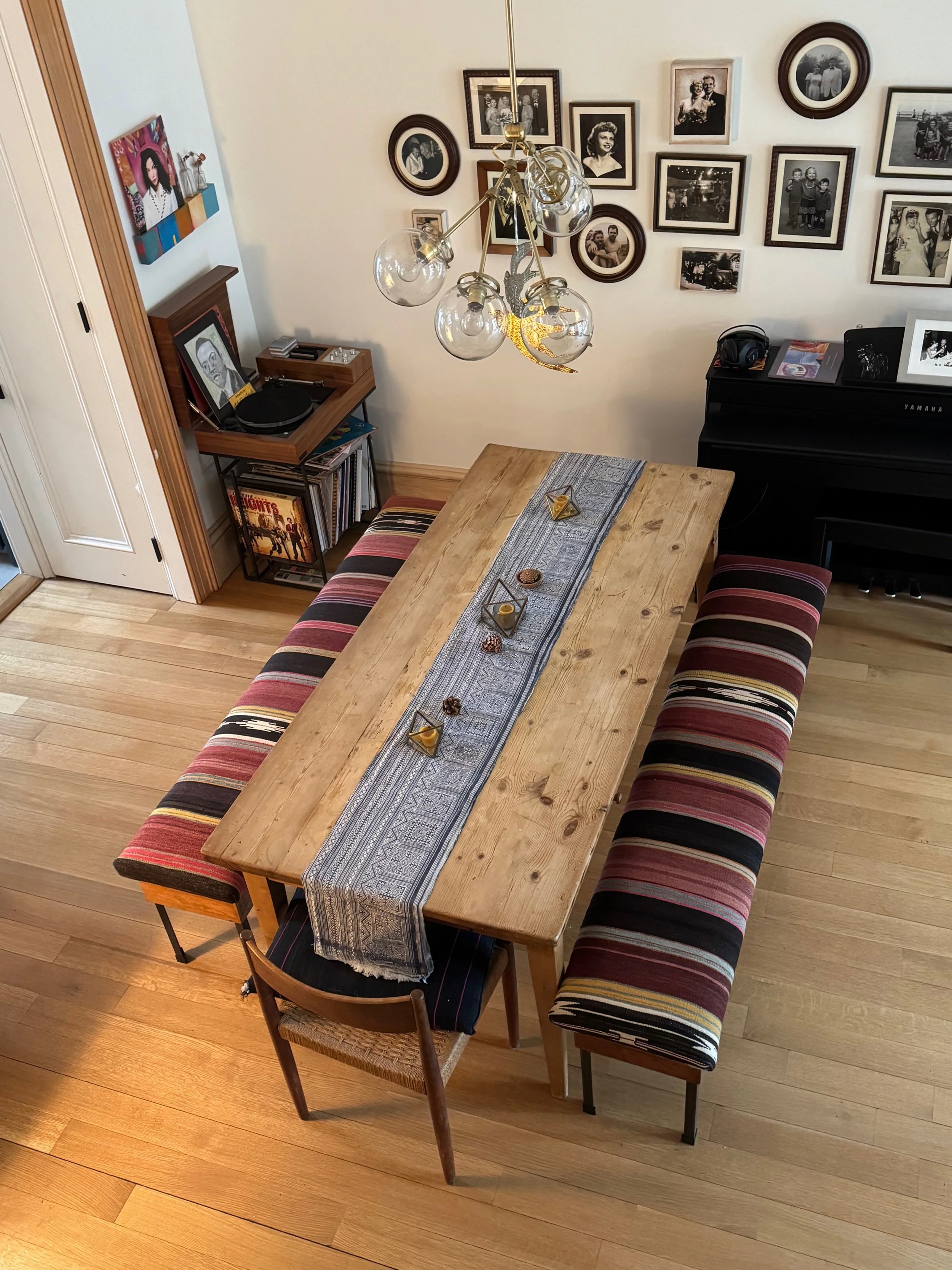 A dining room featuring a custom striped upholstered bench on each side and a single wooden chair at one end, adorned with a gray patterned table runner and decorative objects.