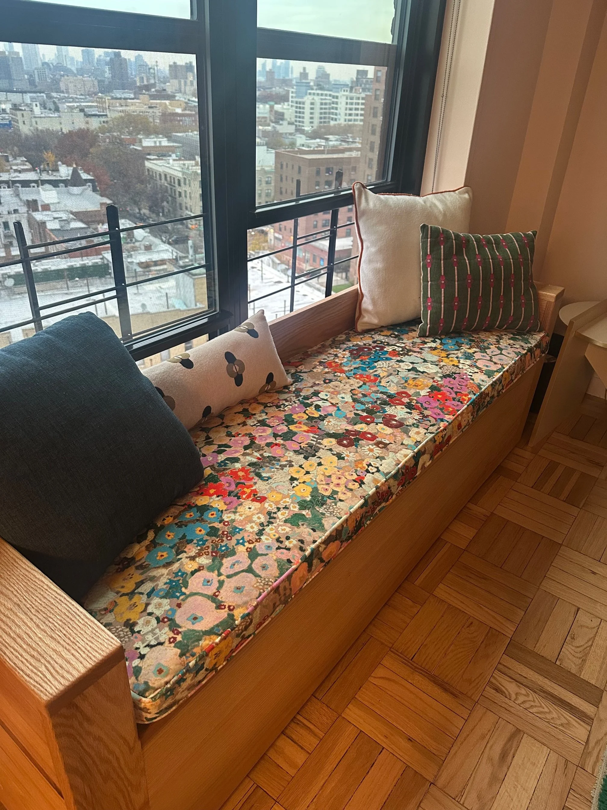 A window seat with a floral cushion and four decorative pillows.
