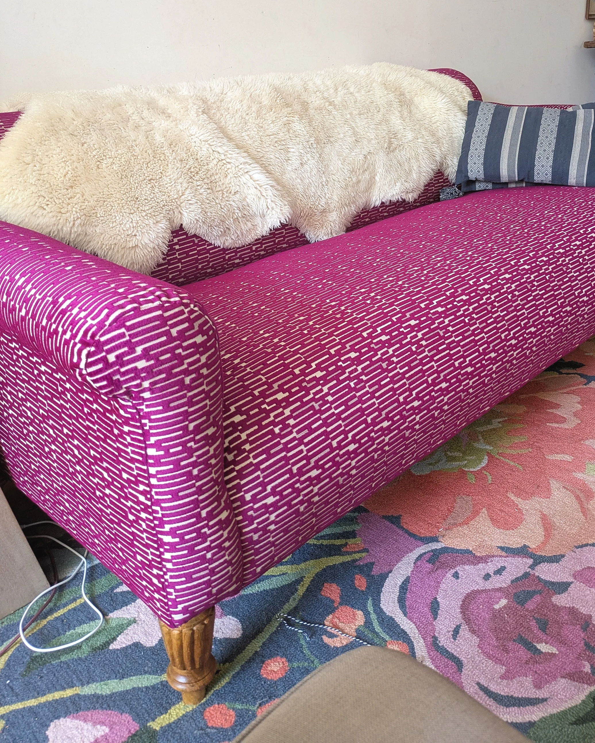 Hot Pink and White Patterned couch in a living room with a rose patterned rug and a lambskin throw