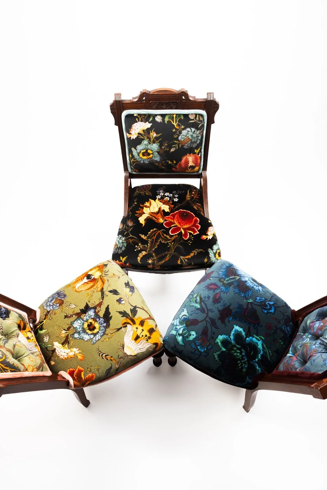 A group of vintage wooden chairs with floral upholstery arranged in a semi-circle, featuring intricate embroidered patterns of flowers and leaves.