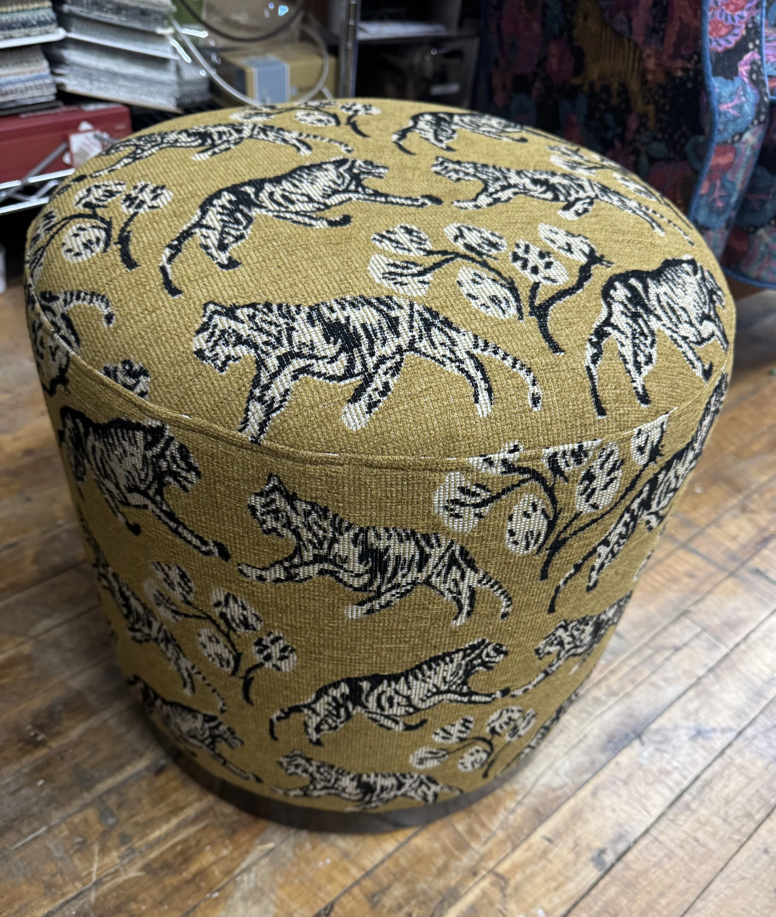 A cylindrical yellow upholstered ottoman with a pattern of black and white zebras and botanical elements, placed on a wooden floor.