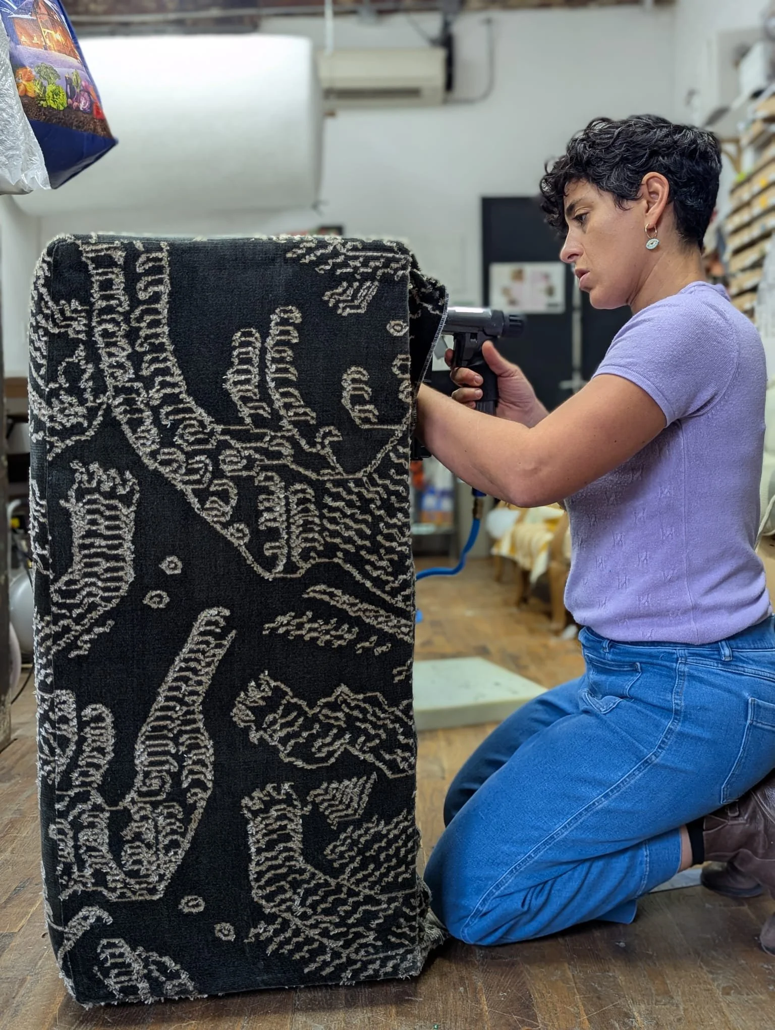 Ruti kneeling and working on a large reupholstery project with the textile pattern displaying skeletal drawings.