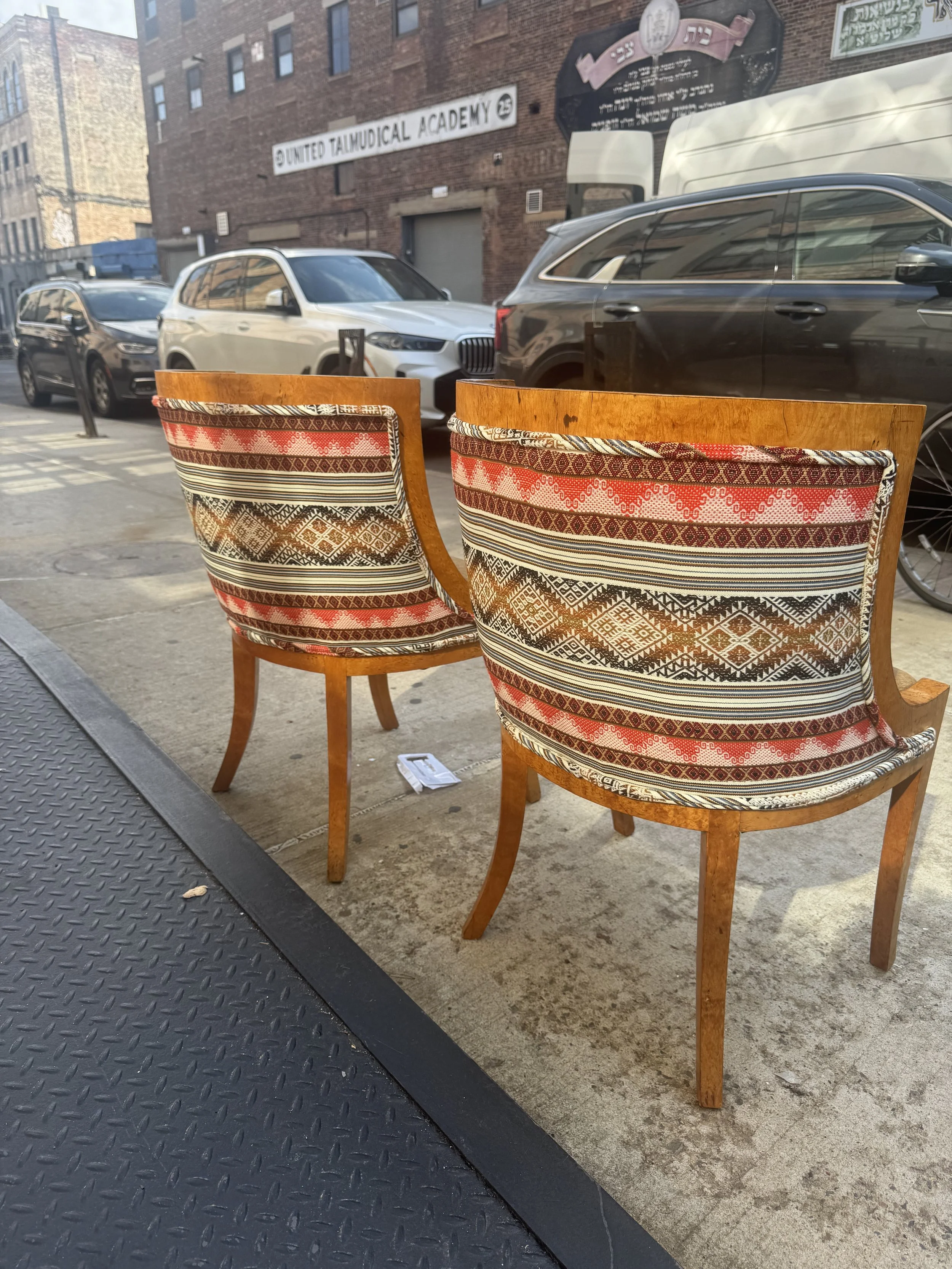 Two wooden chairs with patterned fabric upholstery on a sidewalk in Brooklyn.
