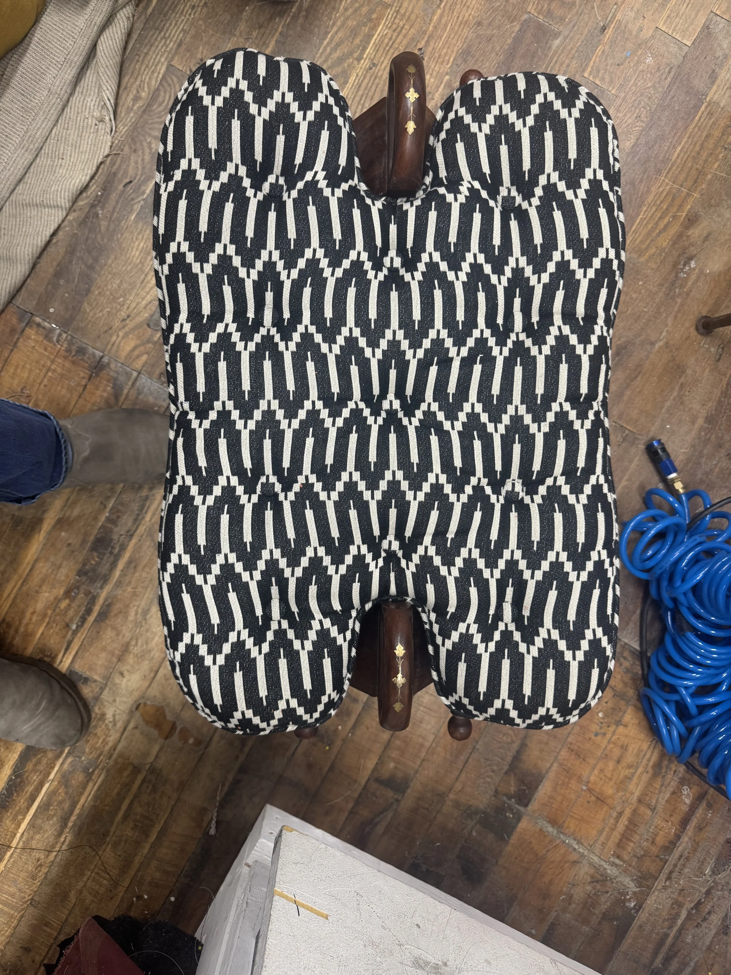 A wooden chair with a black and white geometric patterned fabric cushion on the seat, viewed from above.