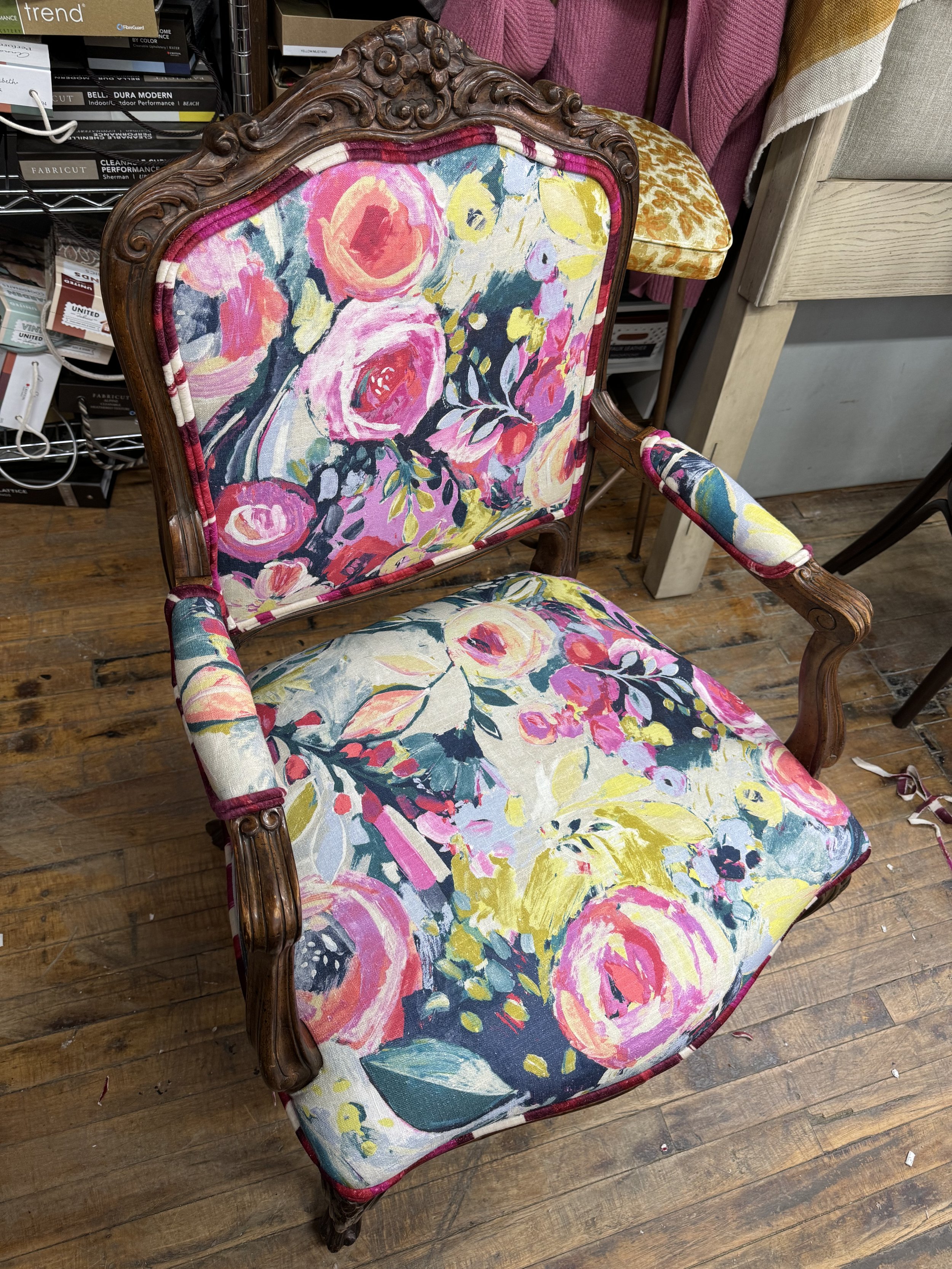 An antique wooden armchair with floral upholstery, featuring pink, yellow, and dark blue flowers on the fabric.