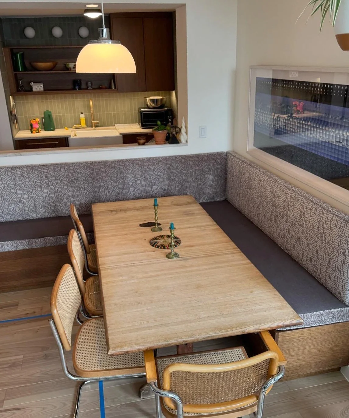 A dining area with a wooden table and four chairs, showcasing a custom built-in upholstered bench with patterned fabric and a long window to the right.