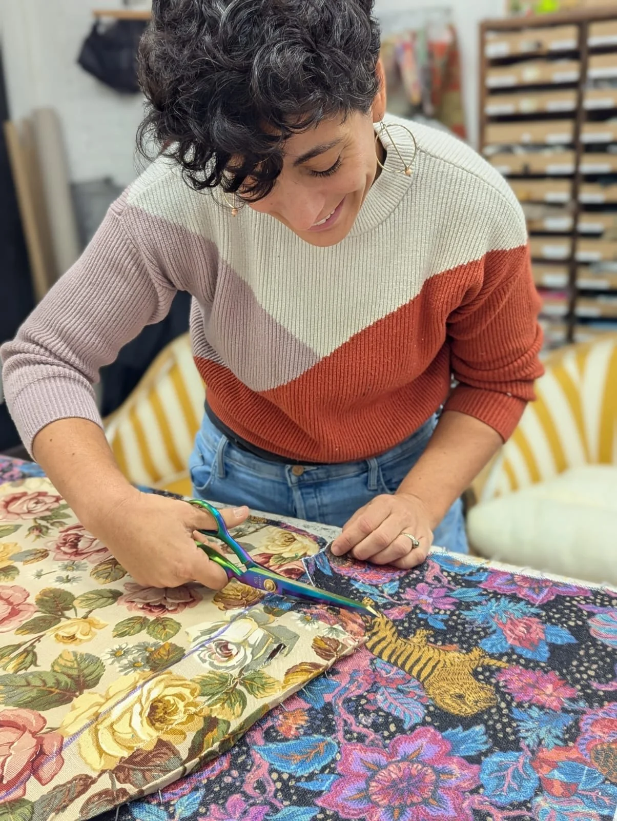 Ruti cutting fabric with scissors on a table with floral patterns.