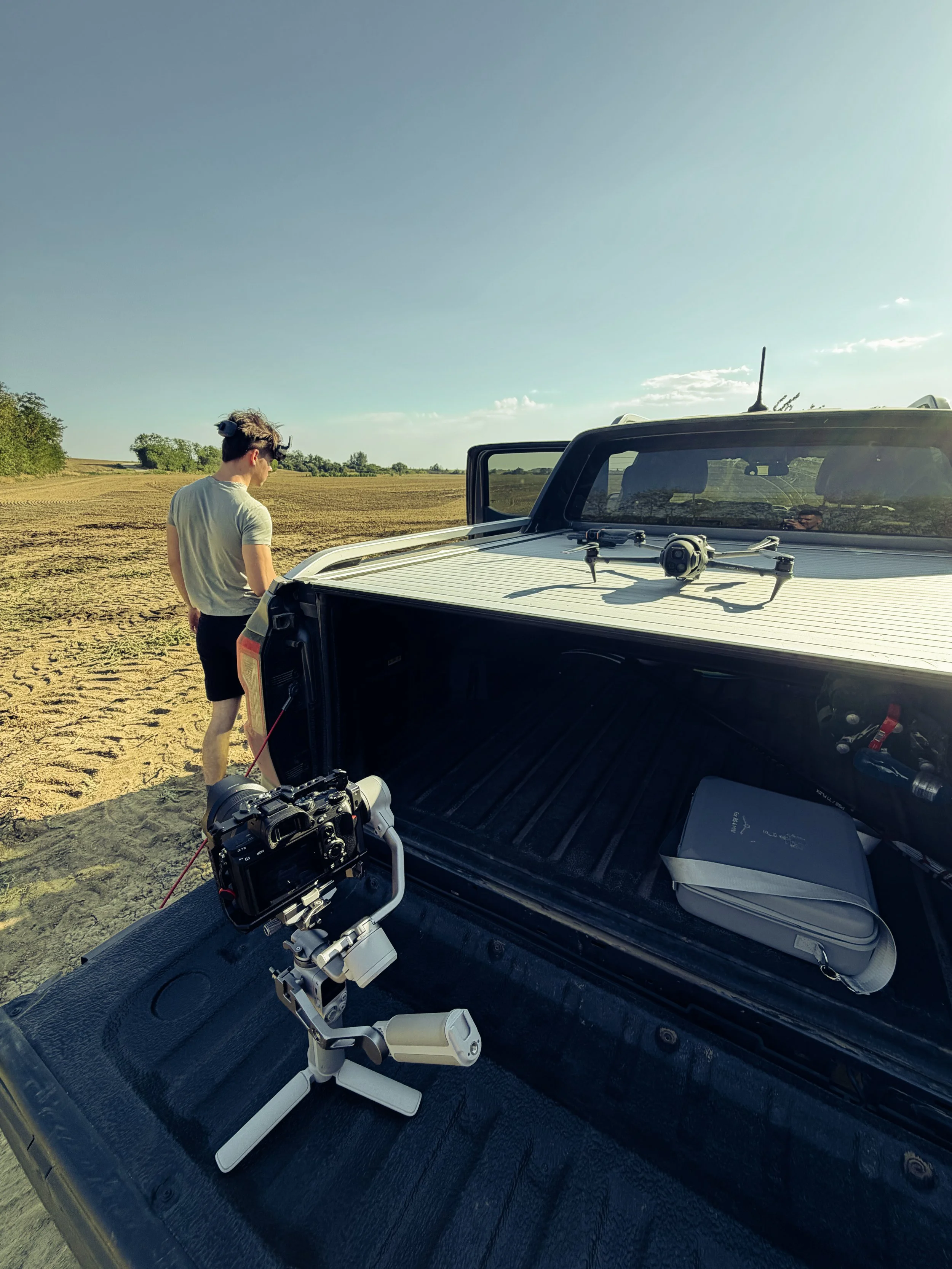 A person with a drone on the back of a pickup truck in a rural field during daytime, with drone equipment on the truck bed.