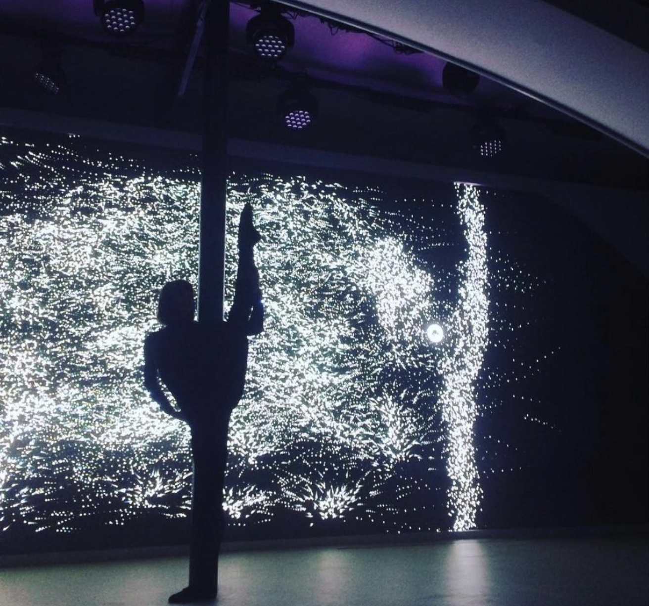 A person dancing silhouette in front of a digital art installation with bright white and purple lights creating intricate patterns. Live show producer, set designer, table scaping, event producer, event consultant, freelance, private, corp, london