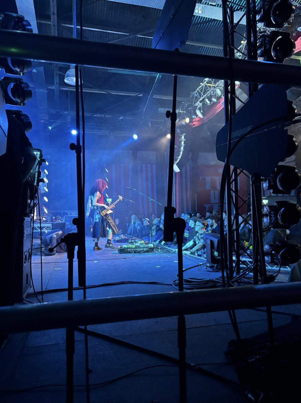 A live music performance on a stage with a guitarist, surrounded by vibrant blue lighting, with an audience watching attentively. Live show producer, set designer, table scaping, event producer, event consultant, freelance, private, corp, london, wor