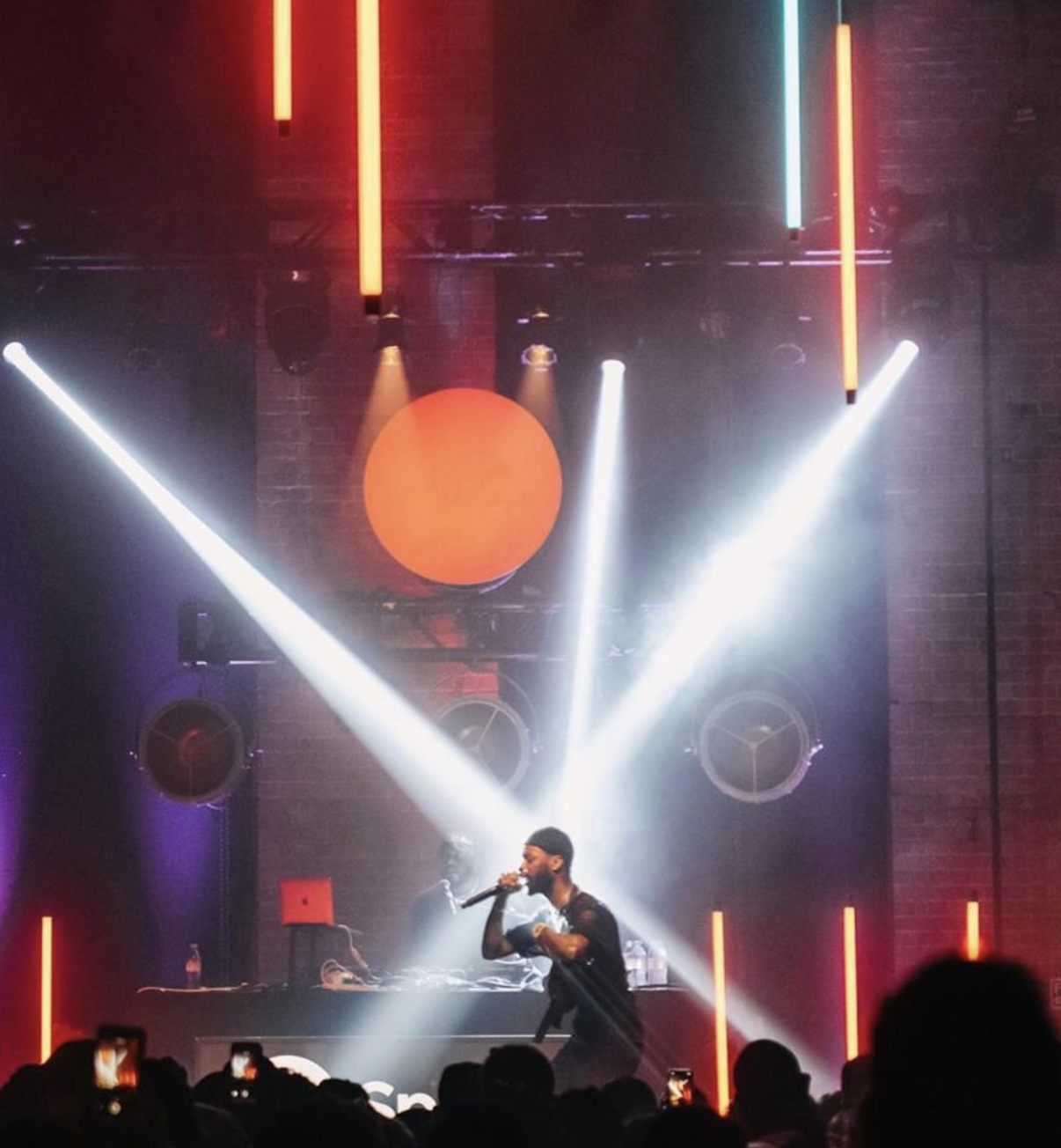 A performer on stage at a concert or club, singing, bright stage lights and a DJ in the background. . spotify. Live show producer, set designer, table scaping, event producer, event consultant, freelance, private, corp, london, worldwide, europe