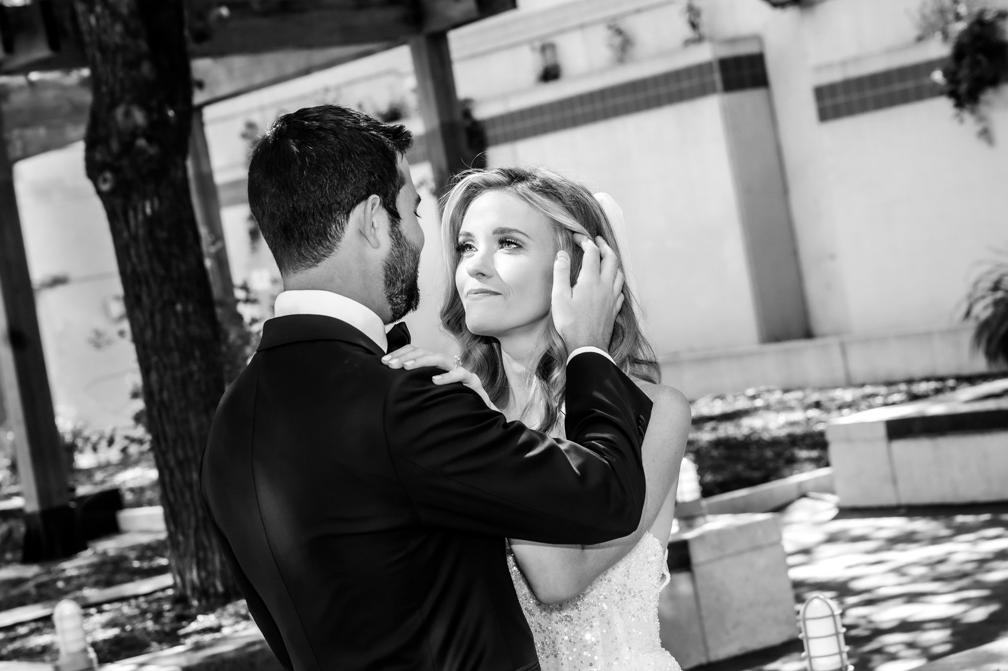 A man in a tuxedo gently holding the face of a woman in a wedding dress, gazing into her eyes.