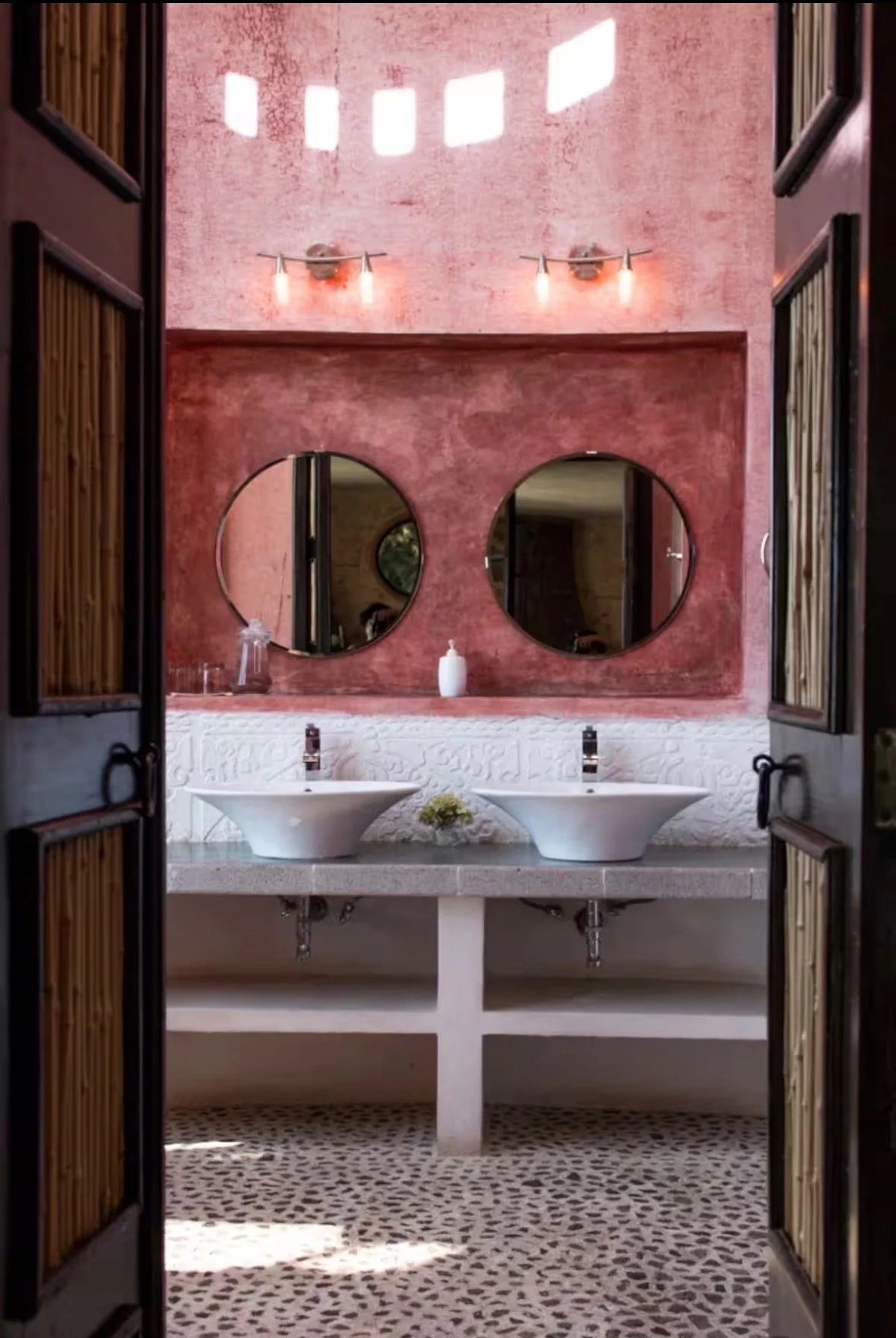 Bathroom with pink textured wall, two round mirrors, and vessel sinks.