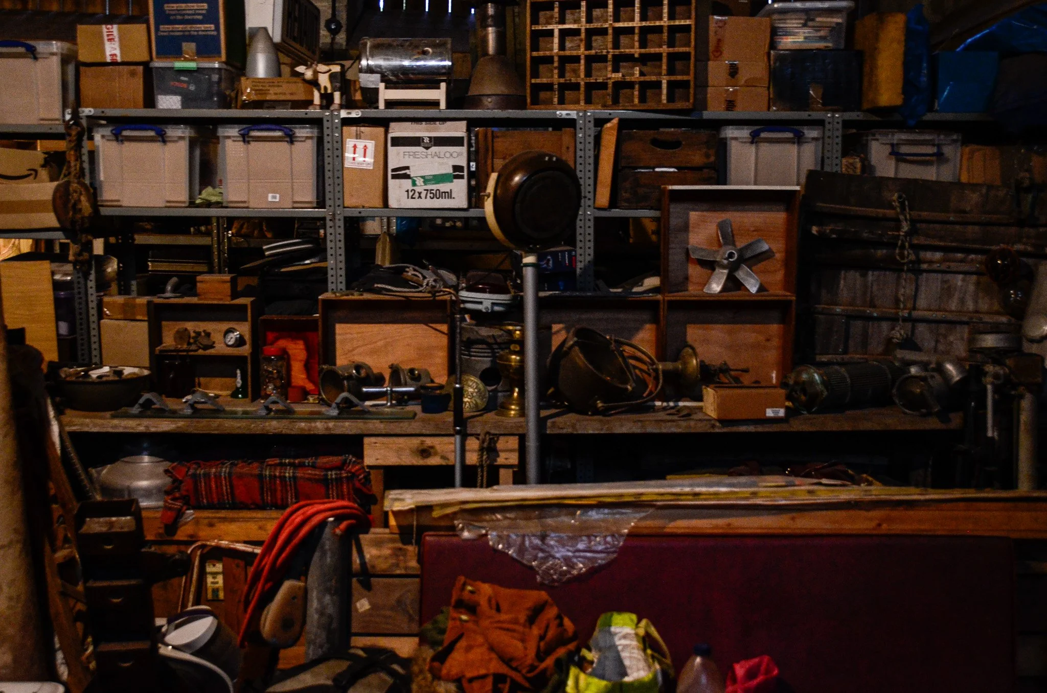 A cluttered storage room with shelves filled with boxes, tools, and miscellaneous items.