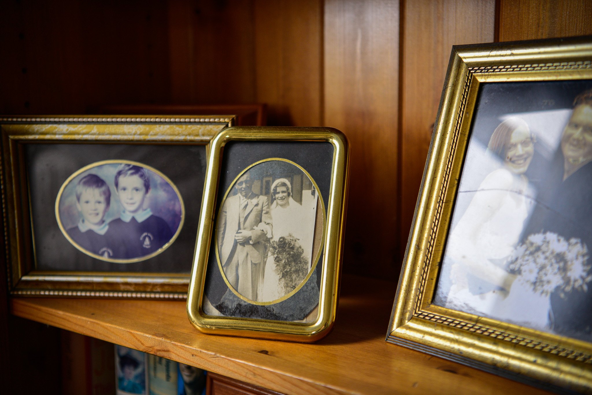 Three framed vintage photographs of people, placed on a wooden shelf with a wood-paneled wall background.