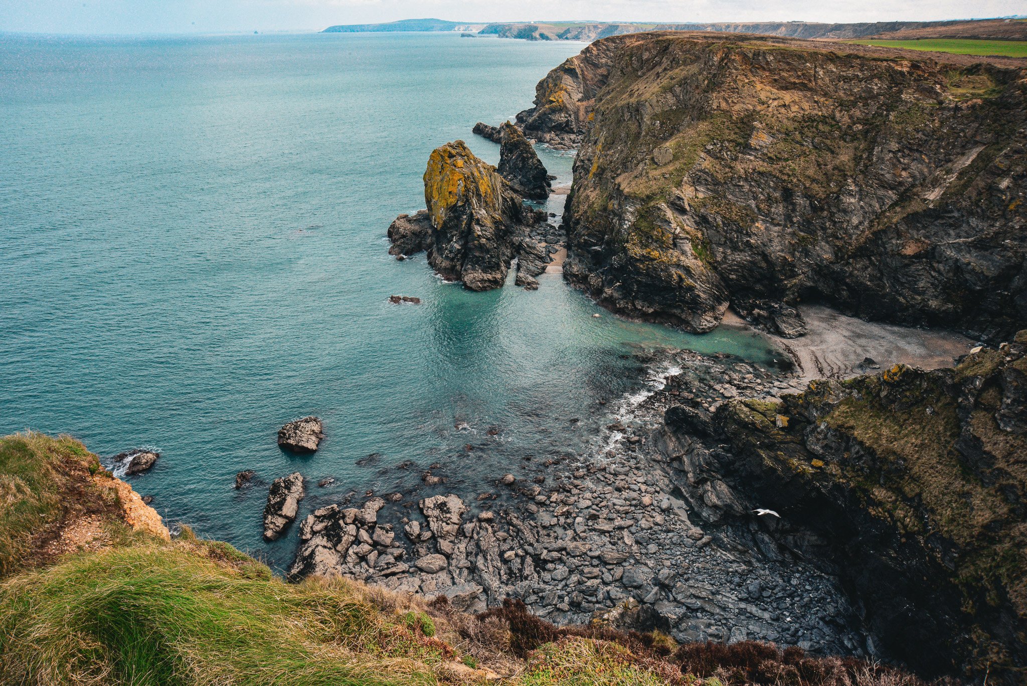 A coastal landscape with steep cliffs, rocky formations, and the ocean extending to the horizon.