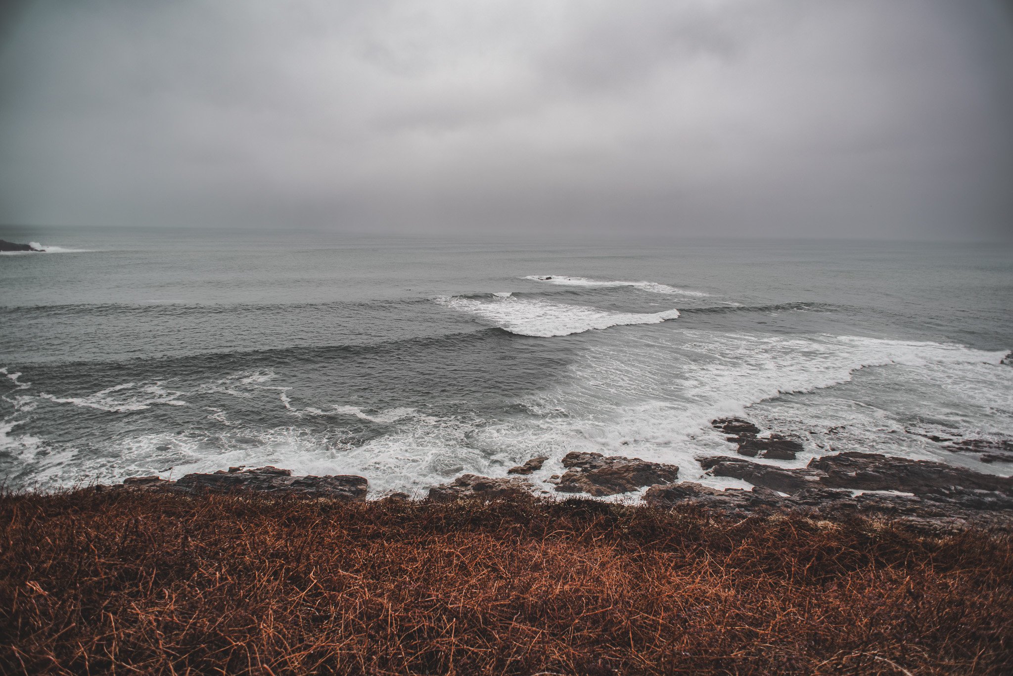 Overcast beach scene with waves crashing on rocky shore and gray sky