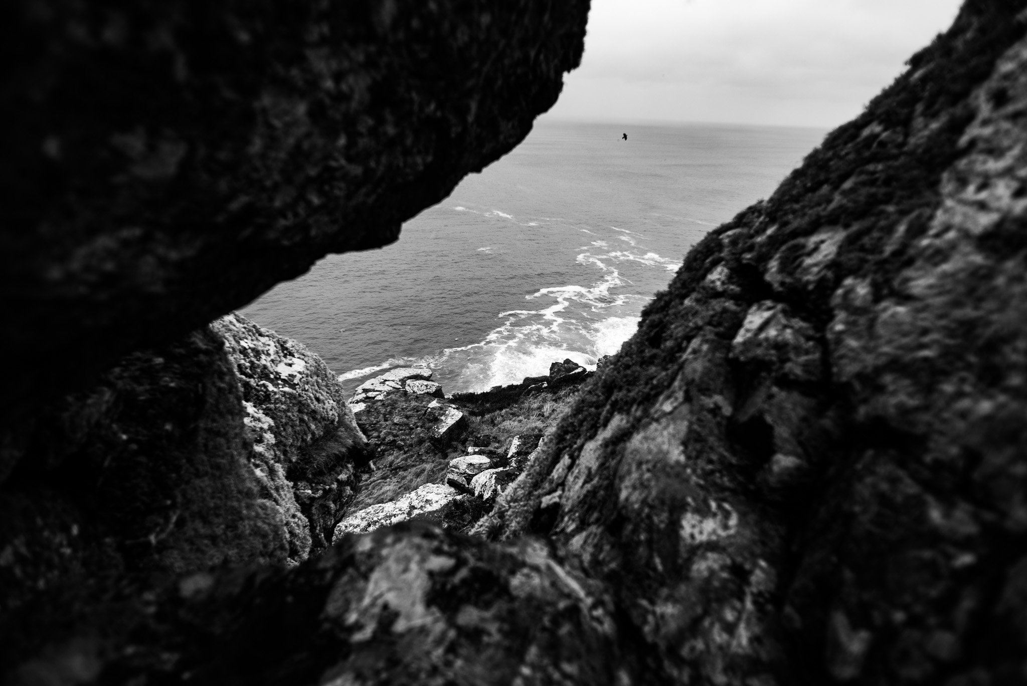 View of the ocean through a rocky fissure, with waves crashing against the rocks, in black and white.