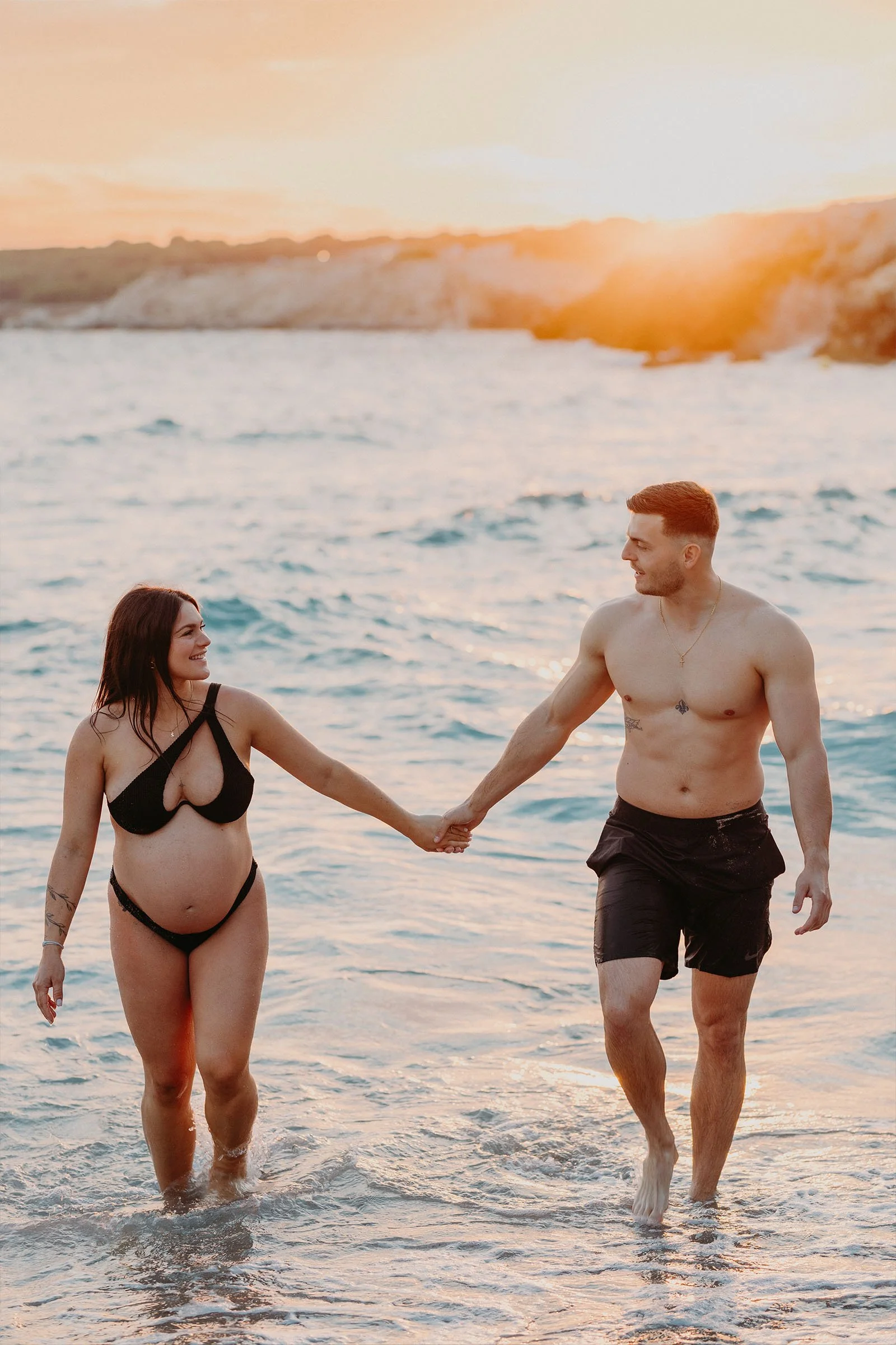 couple de futurs parents marchant main dans la mer au coucher du soleil près de Martigues