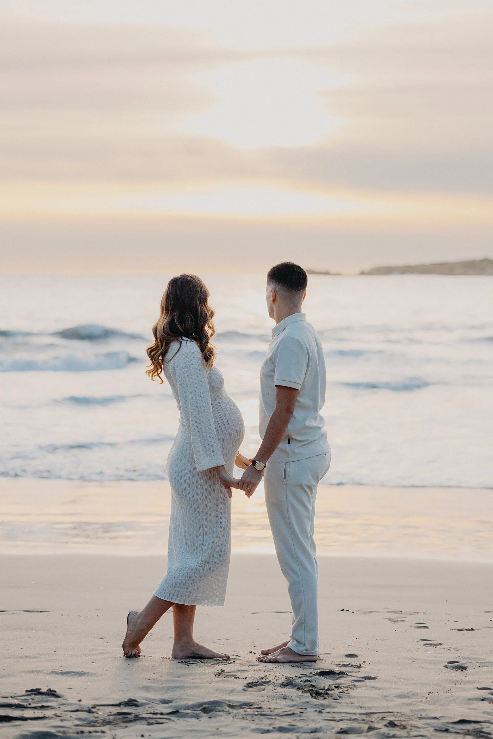 femme enceinte et un homme main dans la main sur la plage au coucher du soleil à Sausset-les-Pins
