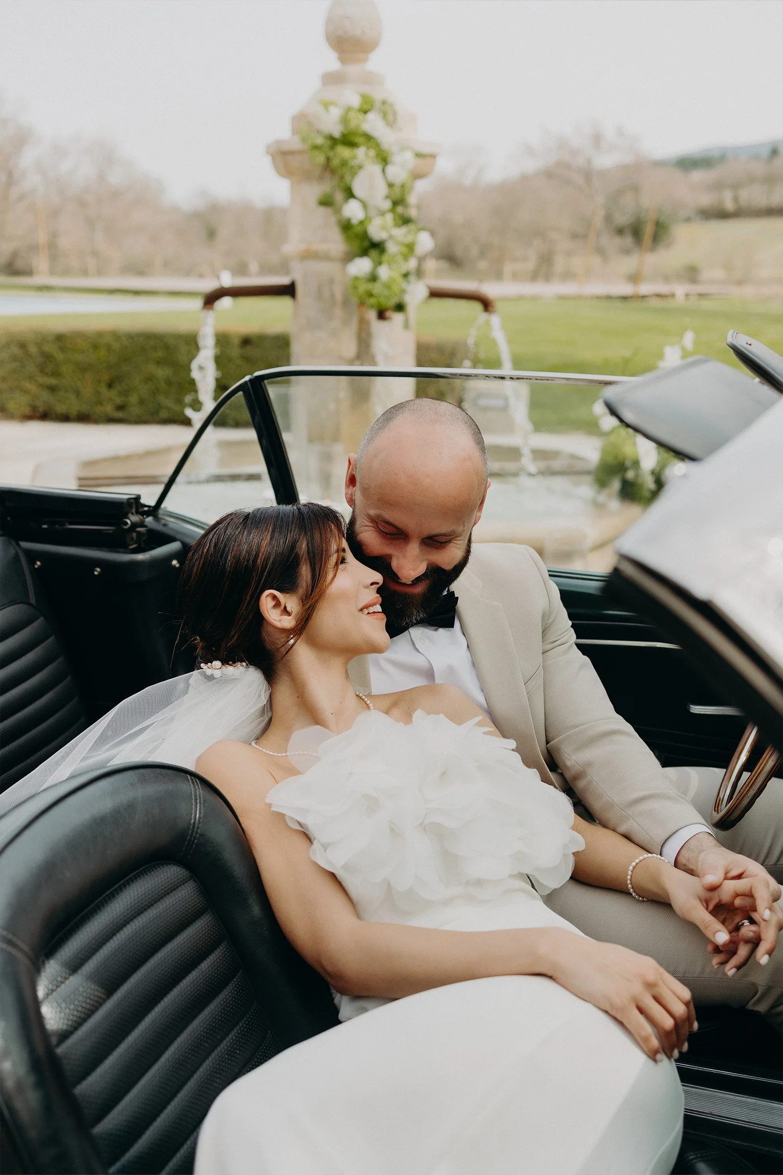 couple en tenue de mariage assis dans une voiture ancienne au Château du Griffon dans le Luberon