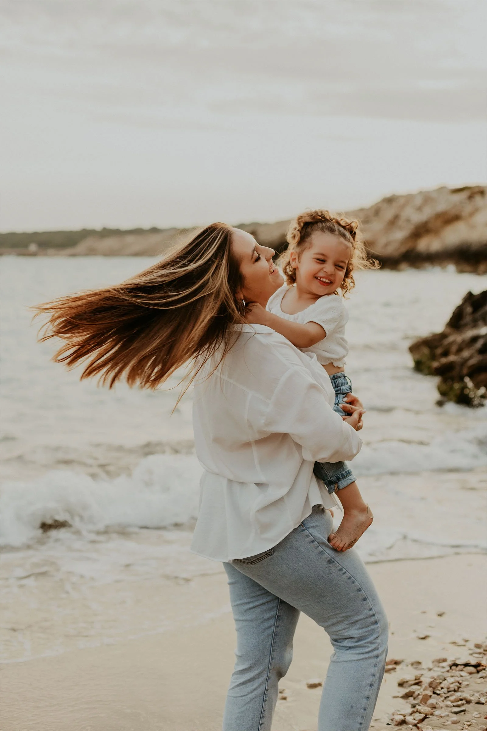 femme souriante tient sa fille dans ses bras sur la plage lors d'une séance photo famille