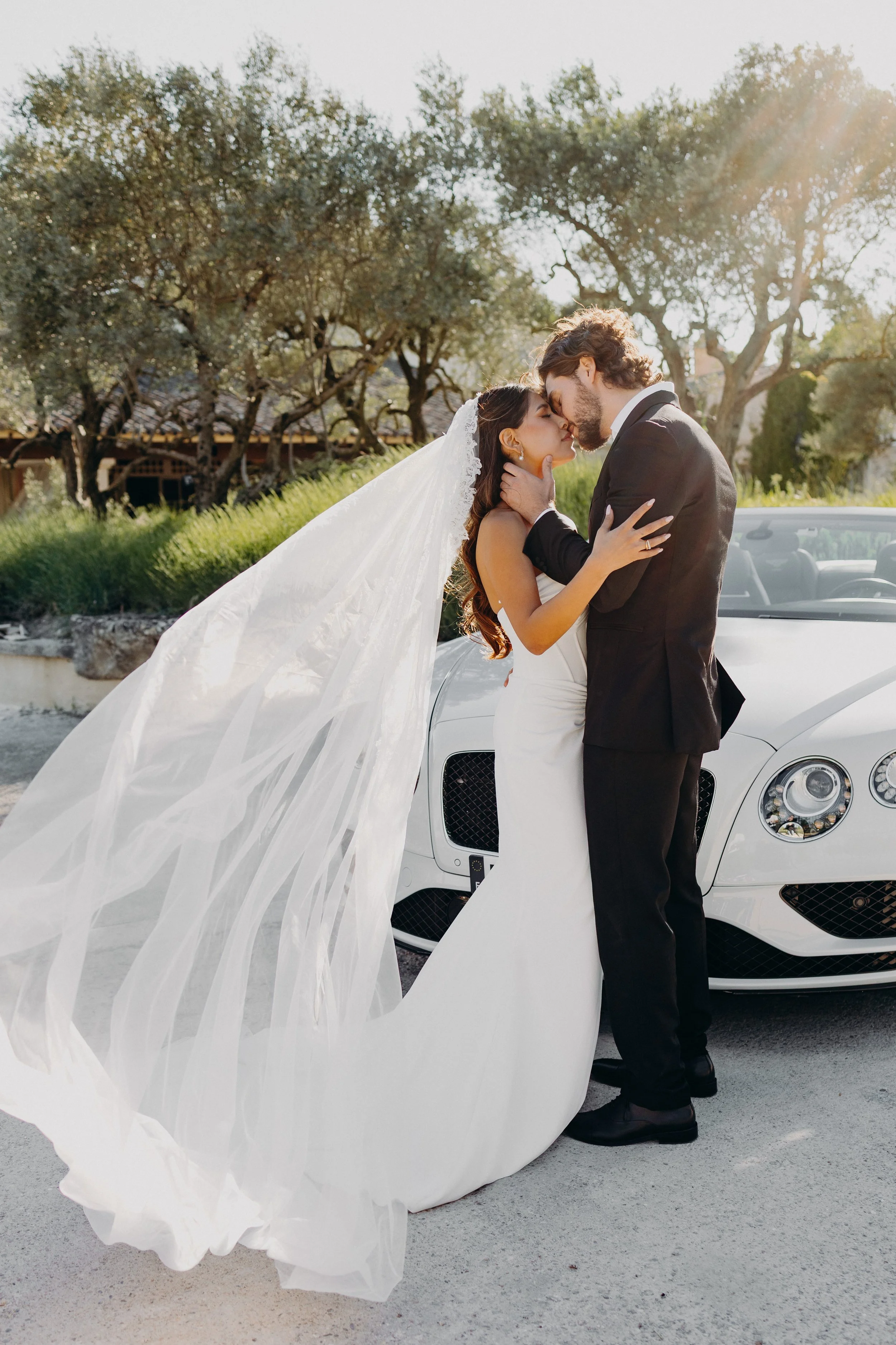 Photo romantique couple de mariés avec voile dans le vent devant une voiture en Provence