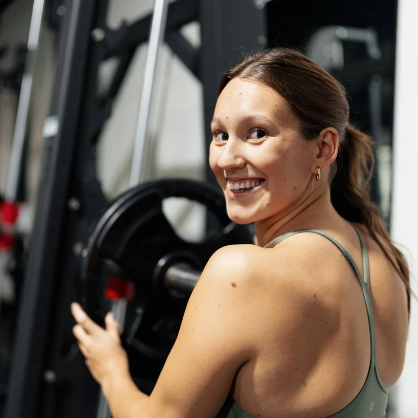 Ella Vrbanac from Ellavate Fitness in London, Ontario smiling back at the camera, adjusting weights on a gym machine.
