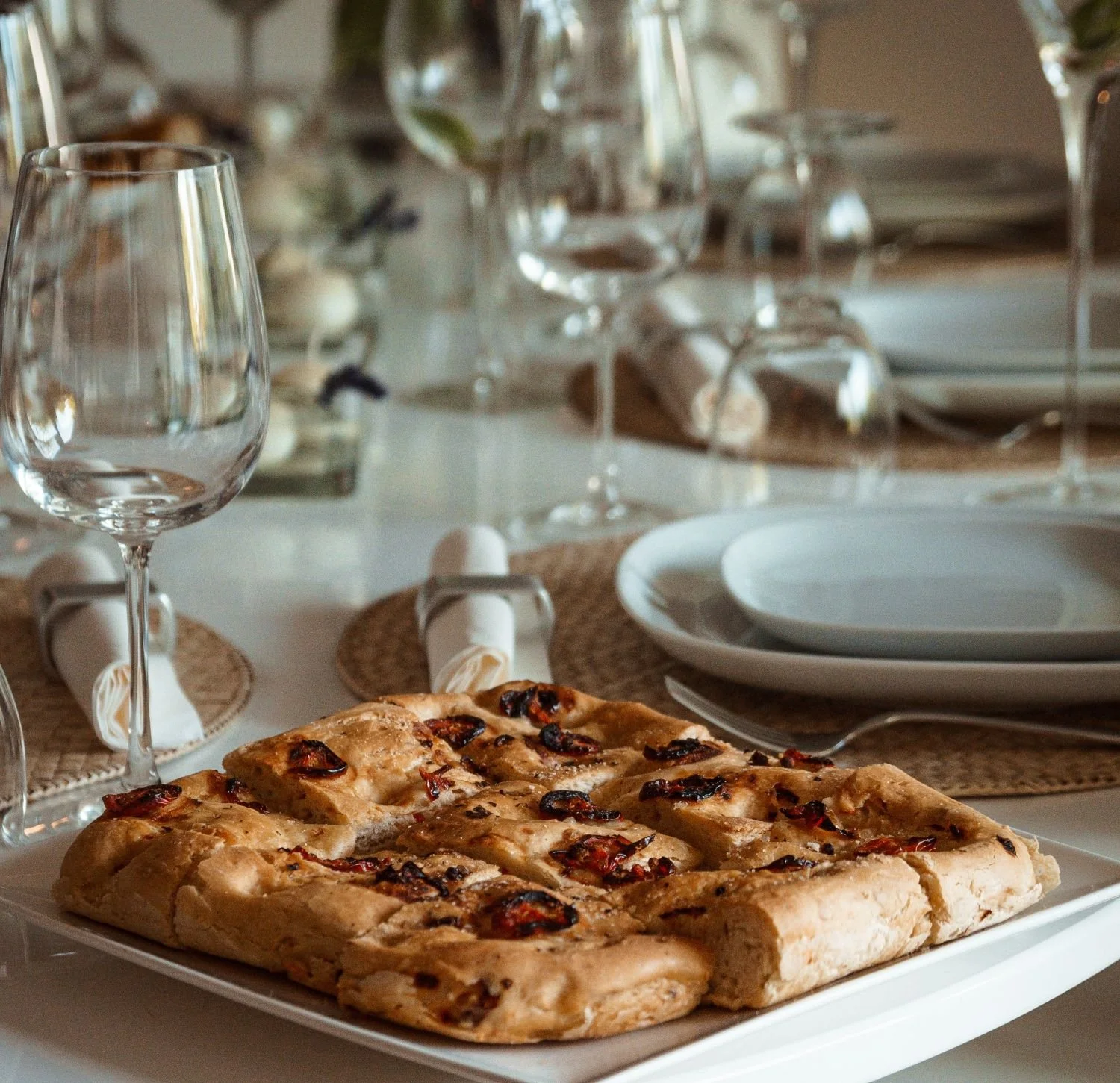 Set dining table with focaccia and wine glasses.