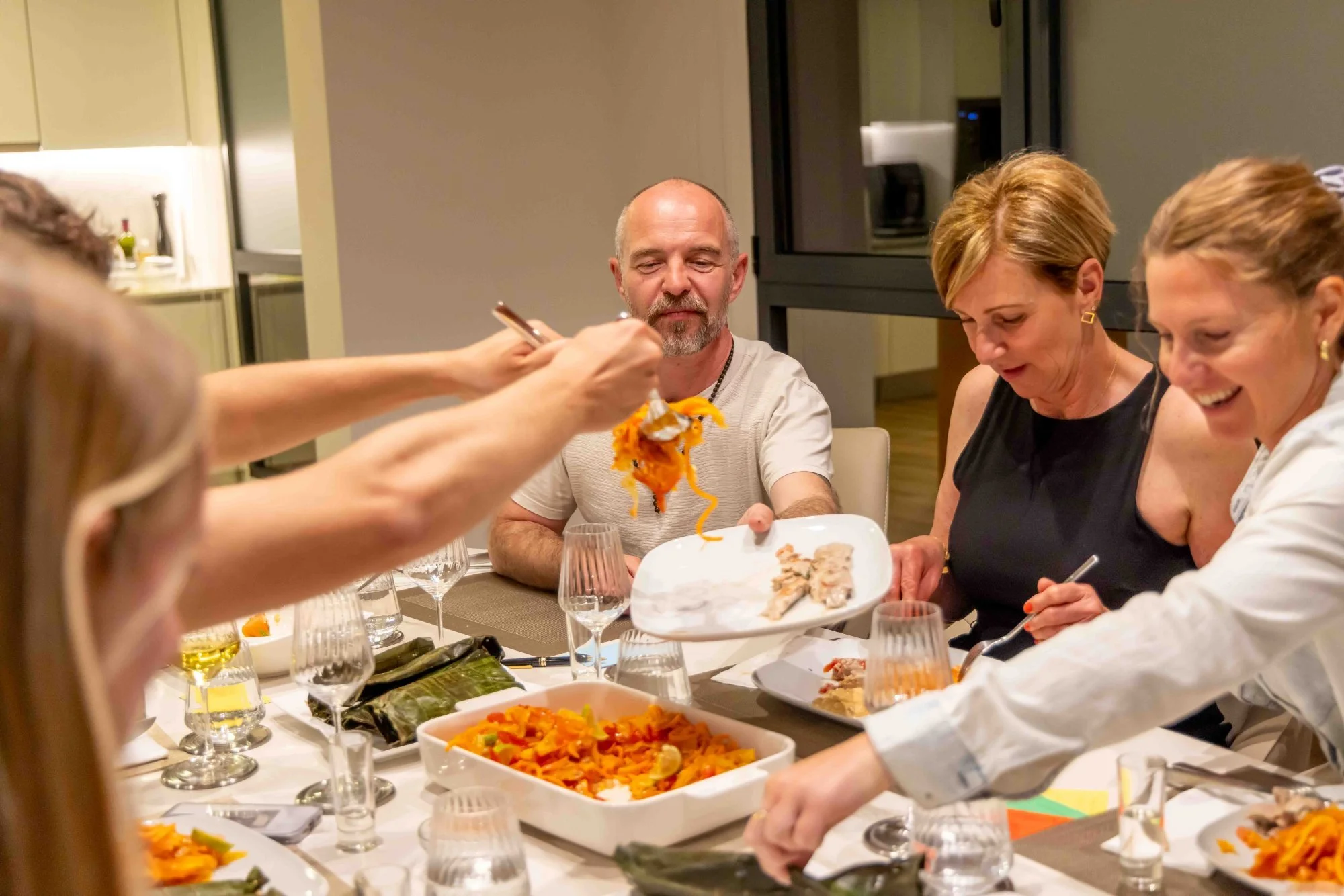 Guests’ hands reaching for the main course at the table.