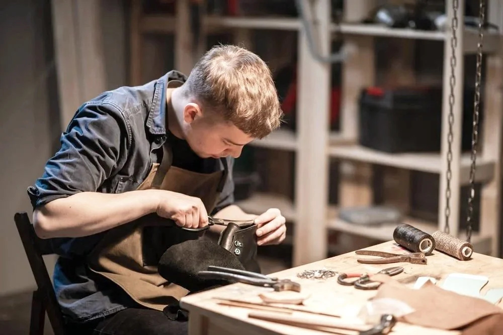 Leatherworker focused on handcrafting leather goods at a work table.