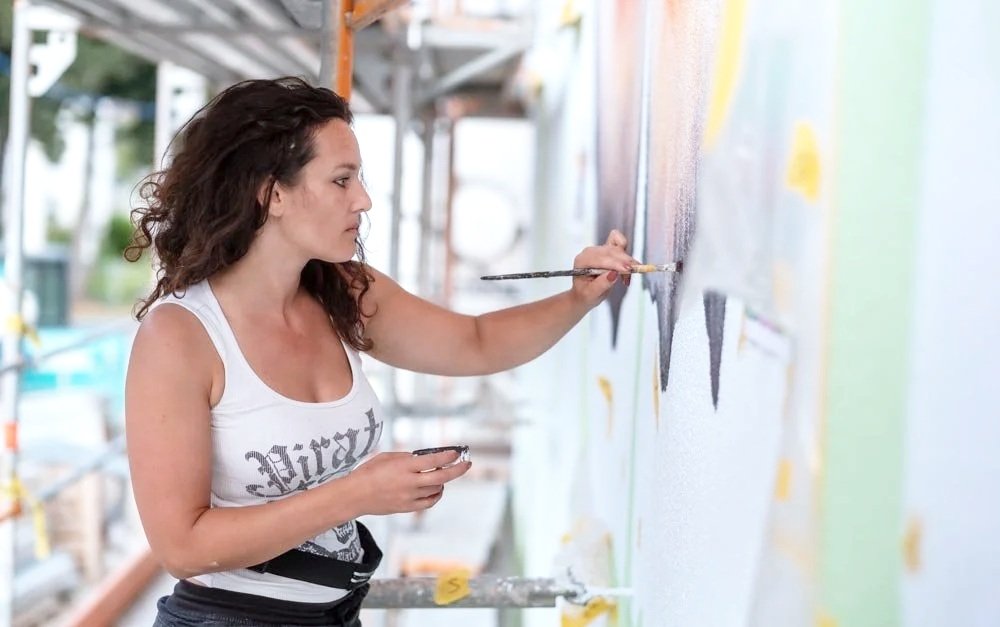 Artist painting a colorful mural on a large wall.