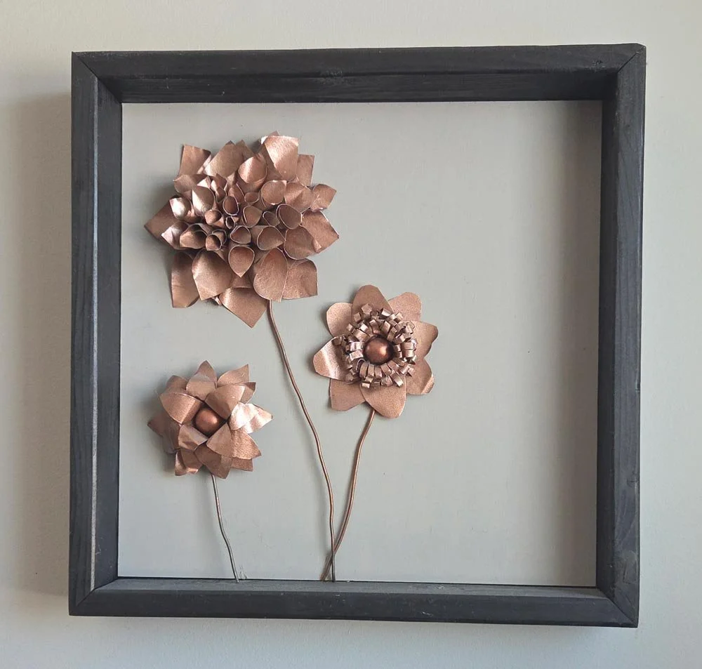 Metal flower wall art created by Christine Caldwell, displayed in a framed shadow box.
