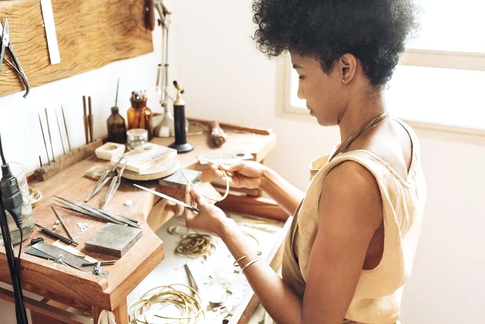 Jewelry maker working with tools at a wooden workbench.