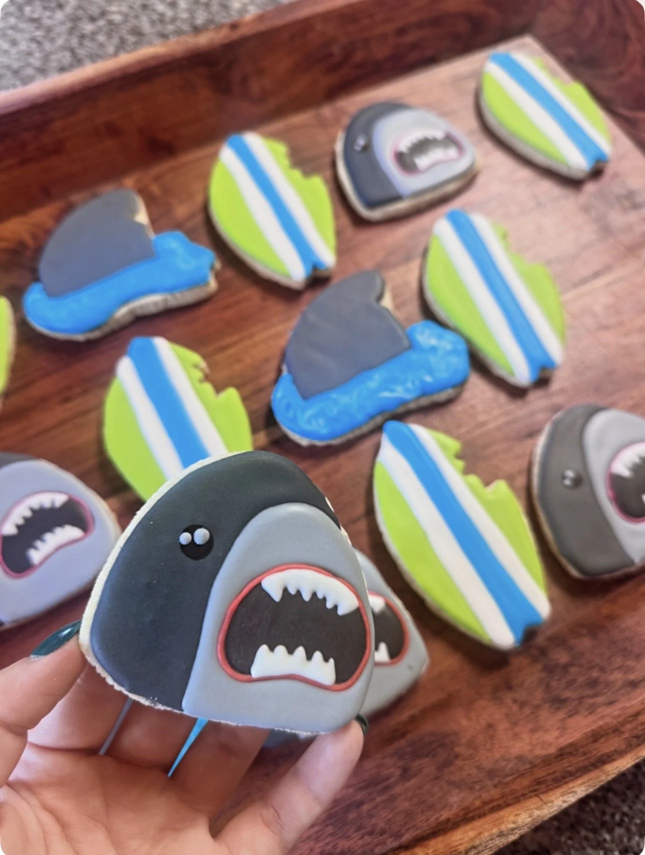 Decorative cookies shaped like sharks and beach scenes with ocean and wave designs, displayed on a wooden surface.