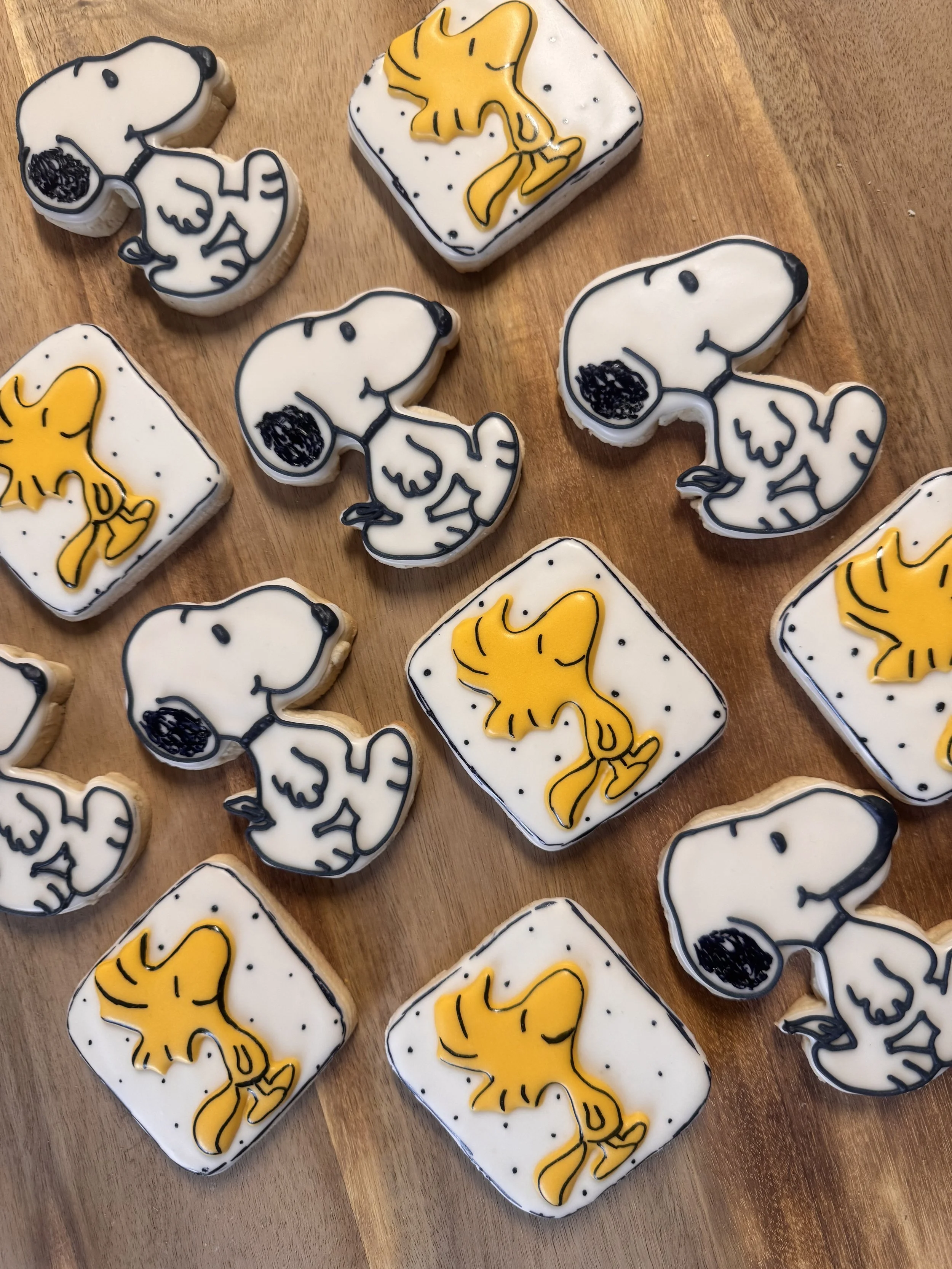 Cookies decorated with Snoopy and Woodstock from Peanuts, placed on a wooden surface.