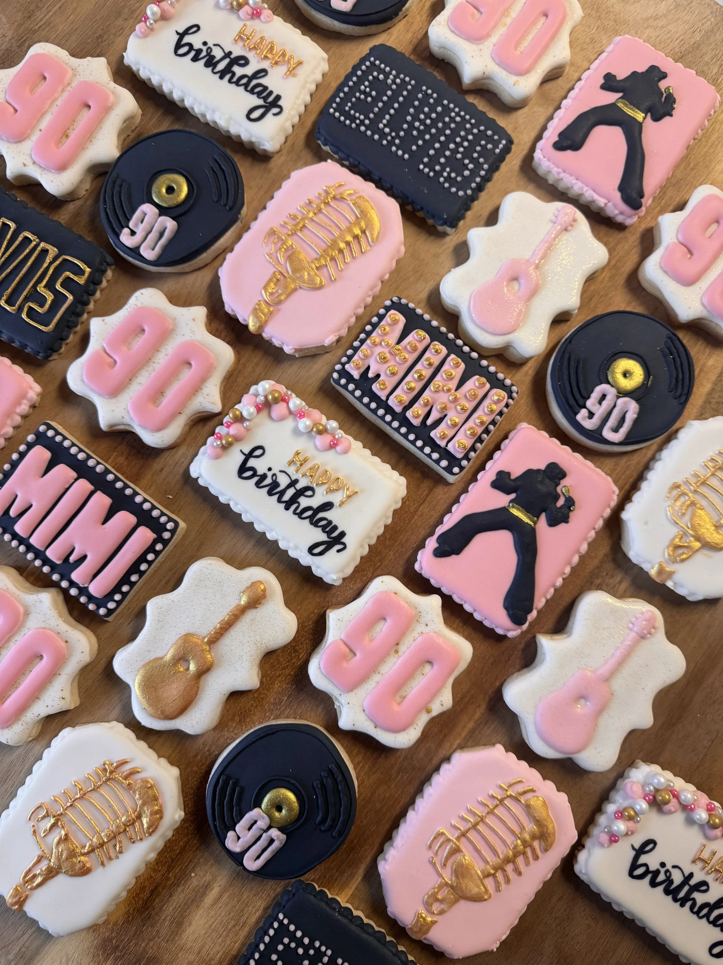 Decorative cookies themed for a 50th birthday celebration, featuring images of guitars, record players, and a martial arts figure, with the numbers '50' and the words 'HAPPY birthday' decorated with pink, black, white, and gold icing.