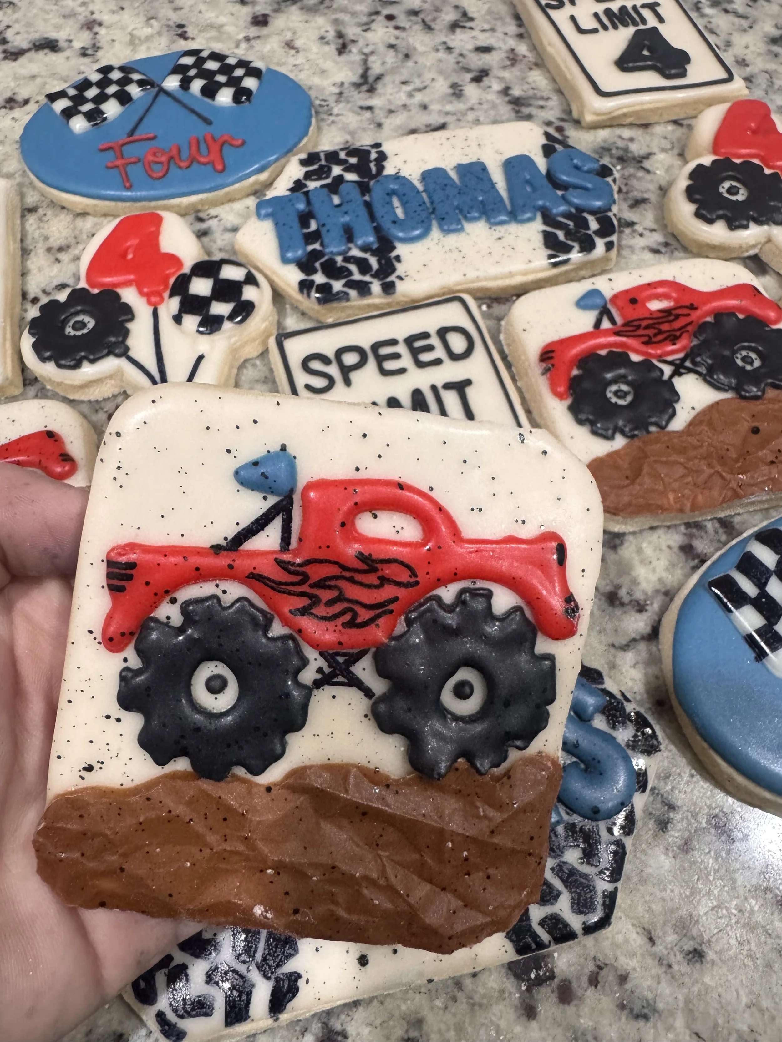 Decorated cookies with racing themes, including a red off-road truck with flames, checkered flags, the name "Thomas," and various signs with racing words like "Speed Limit" and "Four."