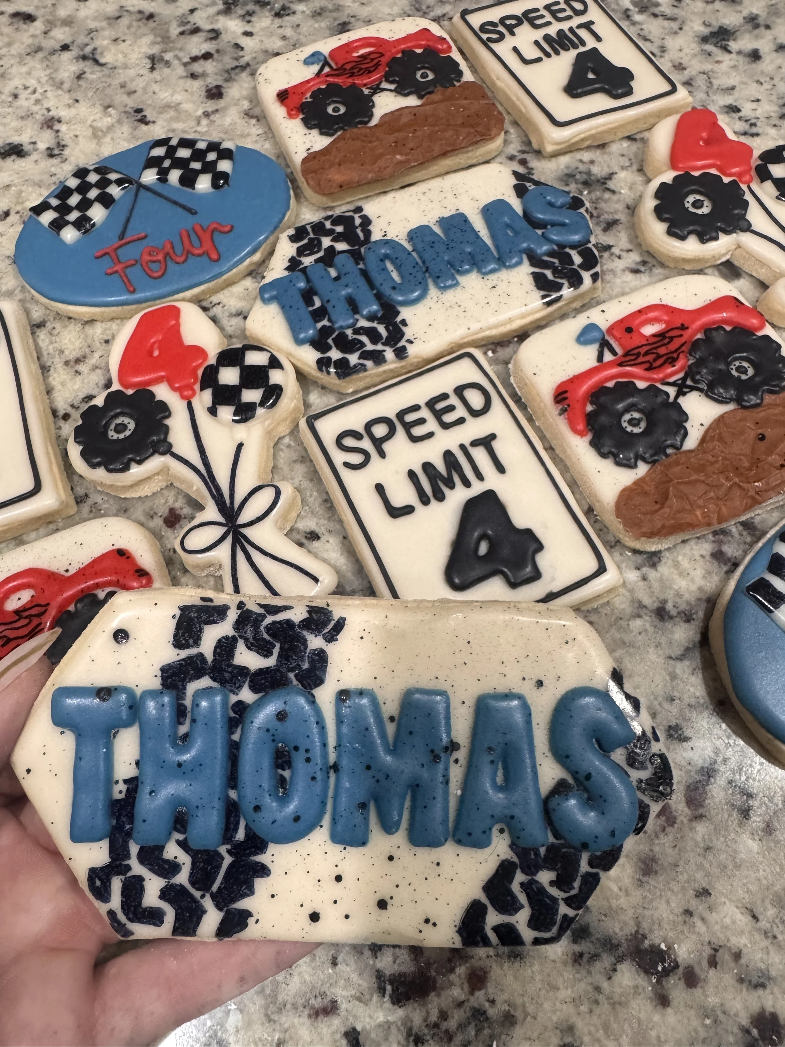Decorative cookies with racing and thank you themes, including cookies with the words 'Thanks,' 'Home,' 'Four,' 'Speed Limit 4,' and race car and checkered flag designs.