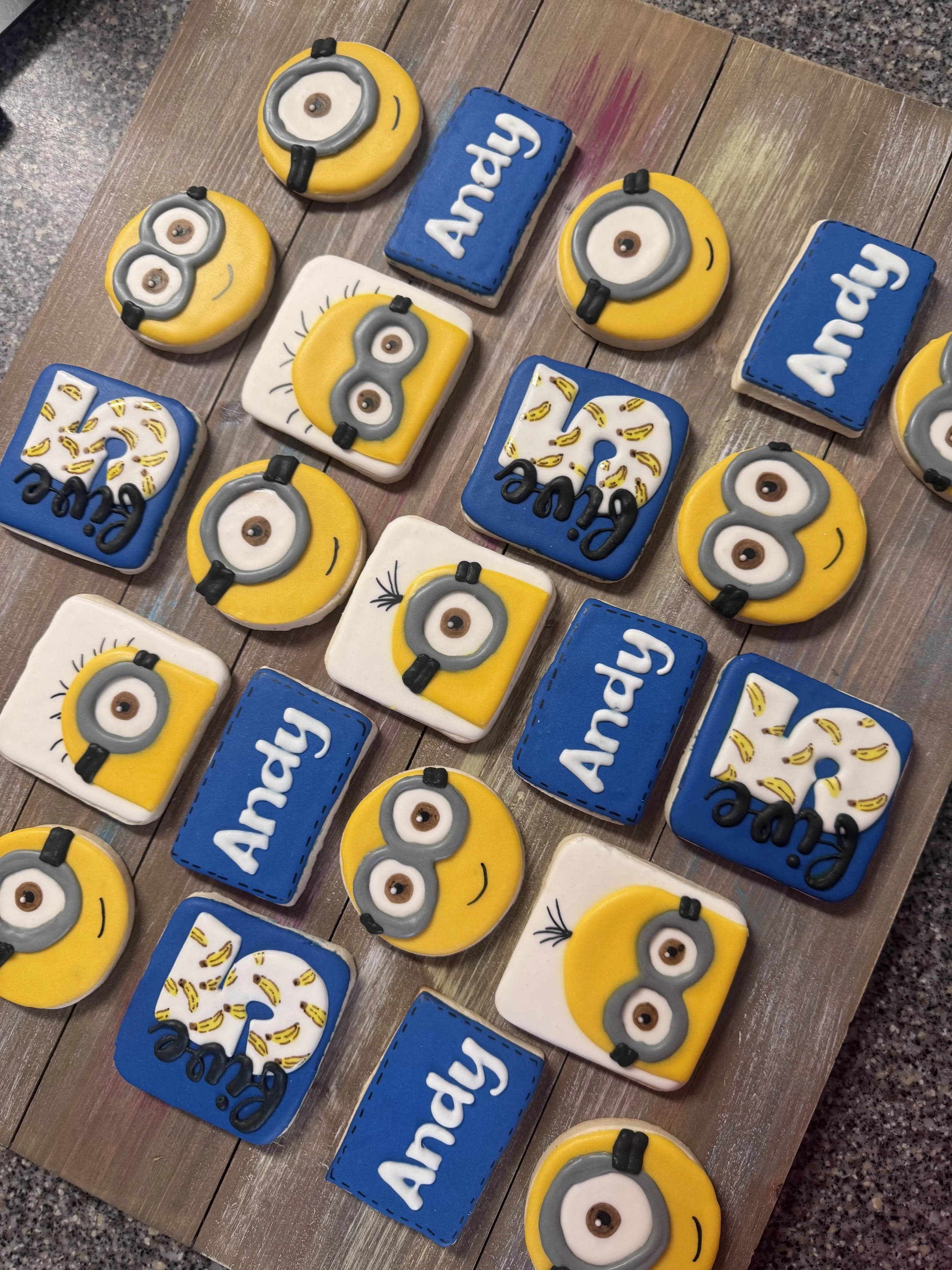 Decorated cookies themed after the movie Minions, featuring Minion faces, goggles, banana patterns, and the word 'Andy'.