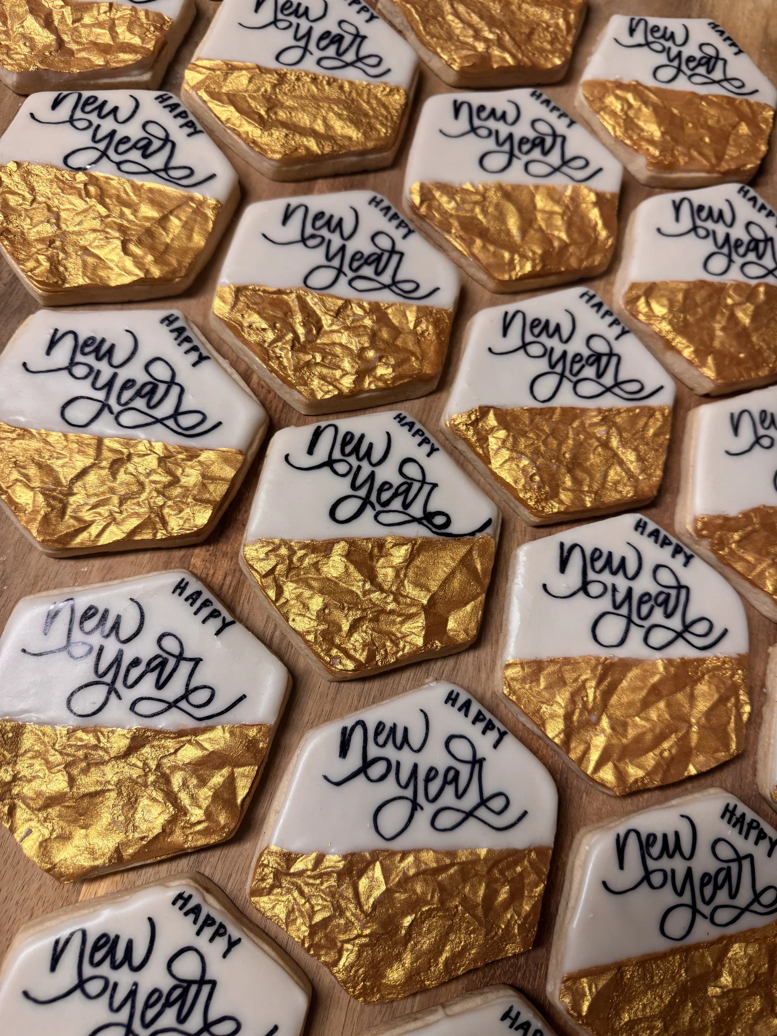 Decorated cookies with white icing and gold leaf, featuring the message 'Happy New Year' written in black, arranged on a wooden surface.