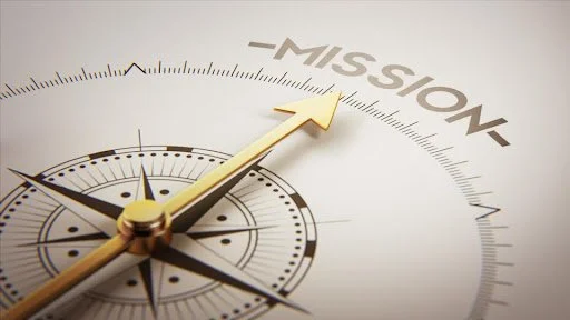 Close-up of a compass with the needle pointing toward the word 'MISSION' on a white background.