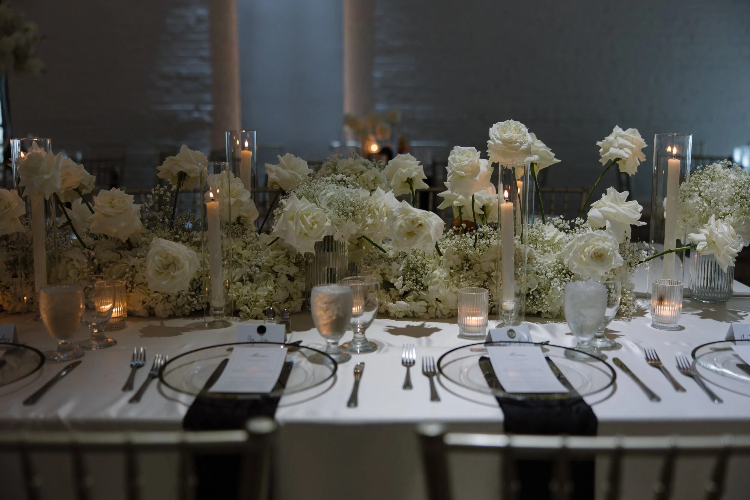 Elegant table setting at a wedding reception with white roses, baby's breath, candles, and glassware.