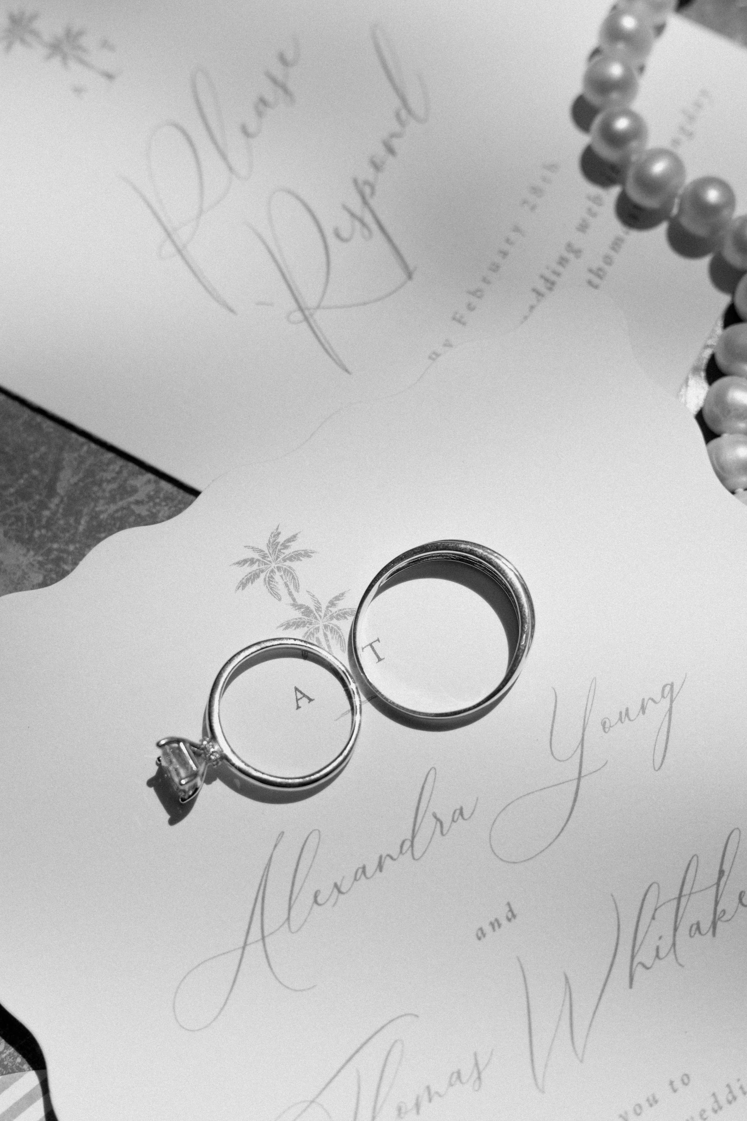 Two wedding rings placed on a letter with handwritten cursive text and a string of pearls.