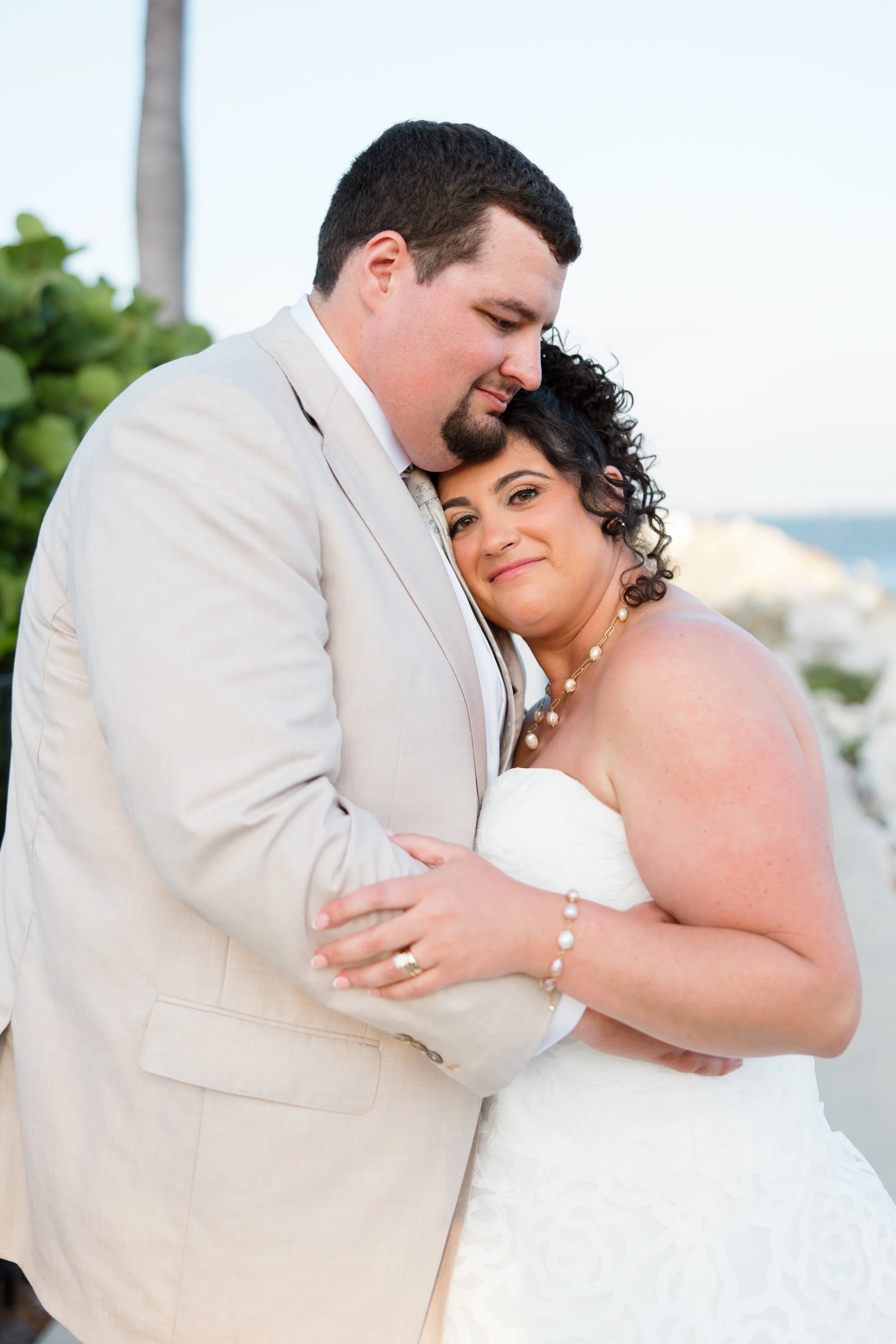 A happy couple embraces on their wedding day with the ocean in the background.